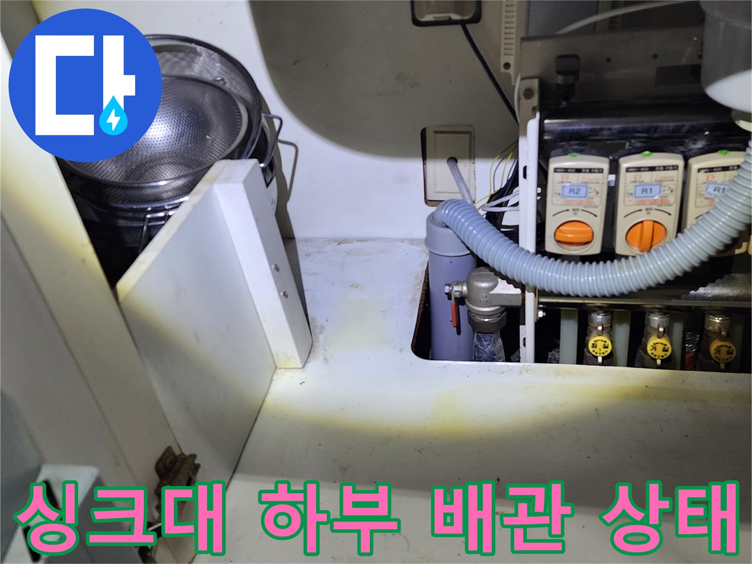 싱크대 하부장 내부의 복잡한 배관과 연결 호스 모습