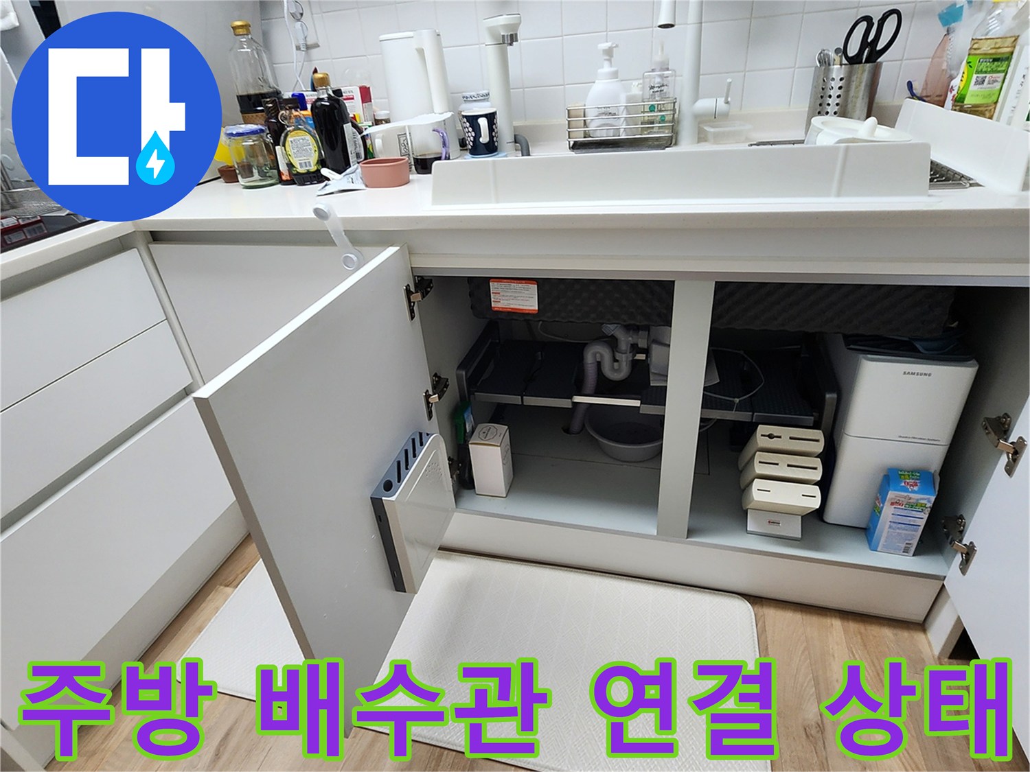 싱크대 하부장 내부에 노출된 배수 호스와 바닥 매립 부위의 모습