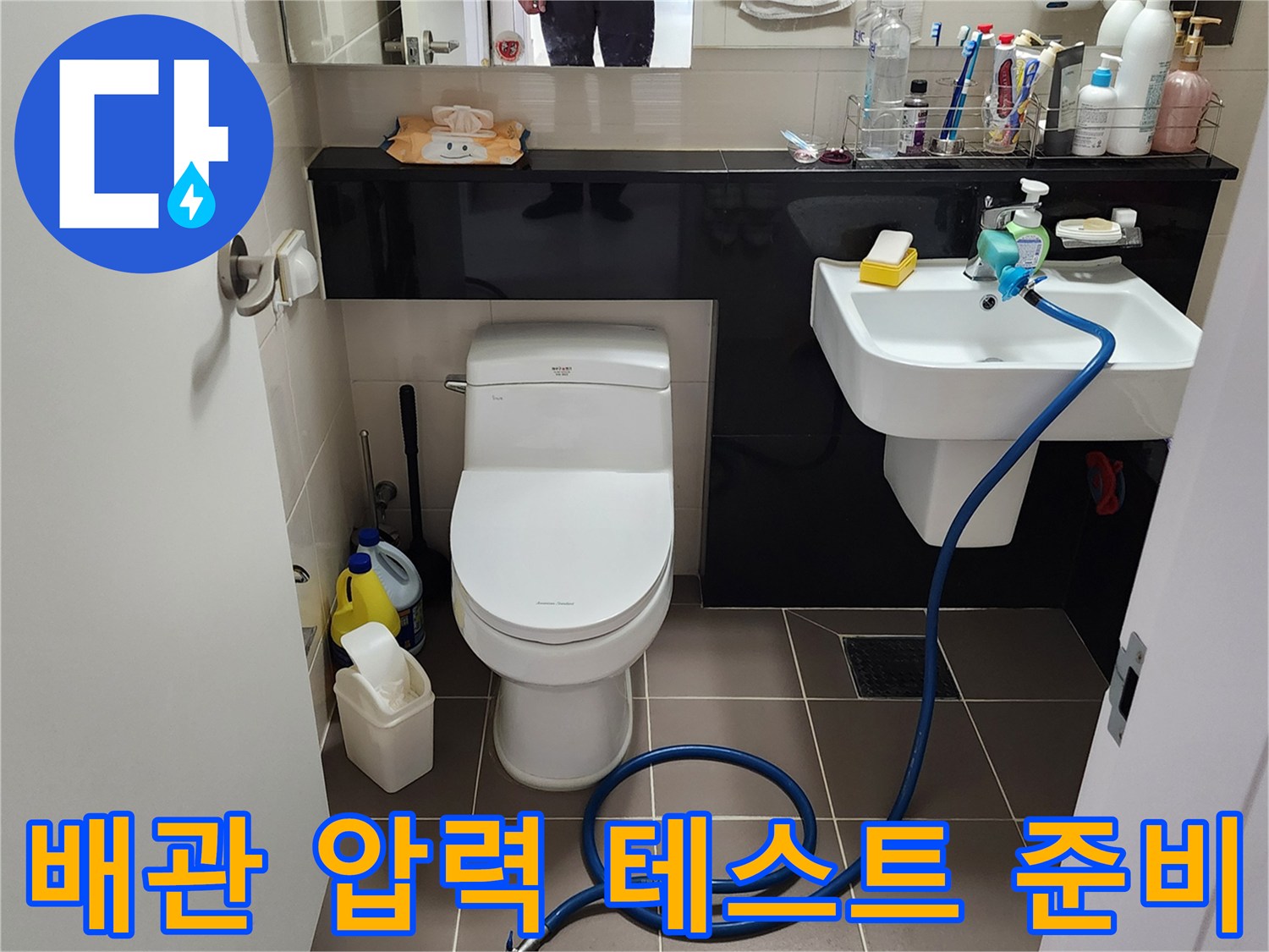 화장실 세면대 아래 배관에 누수 탐지용 호스를 연결하여 점검하는 엔지니어의 작업 모습