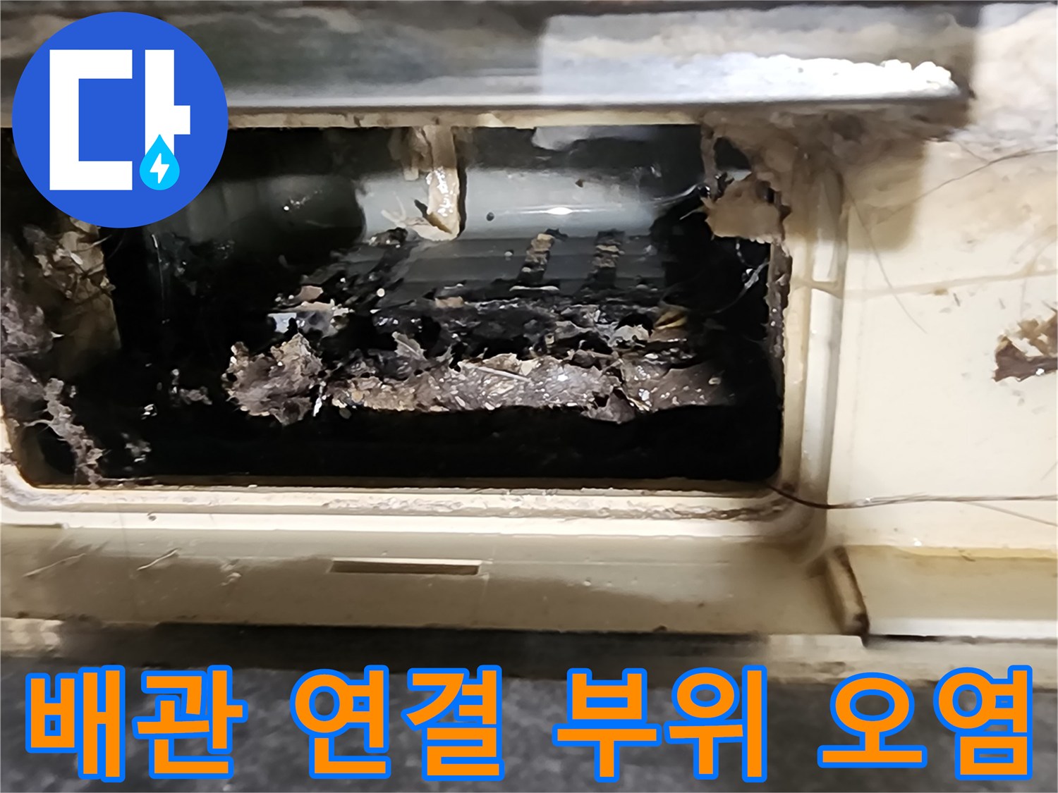 배수관 연결부 주변에 젖은 이물질과 찌꺼기가 엉겨 붙어 있습니다.