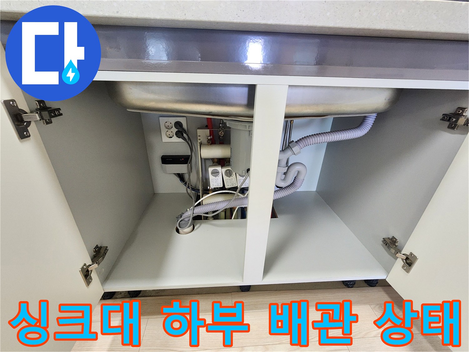 주방 싱크대 하부장 내부의 배관과 전기 콘센트 모습
