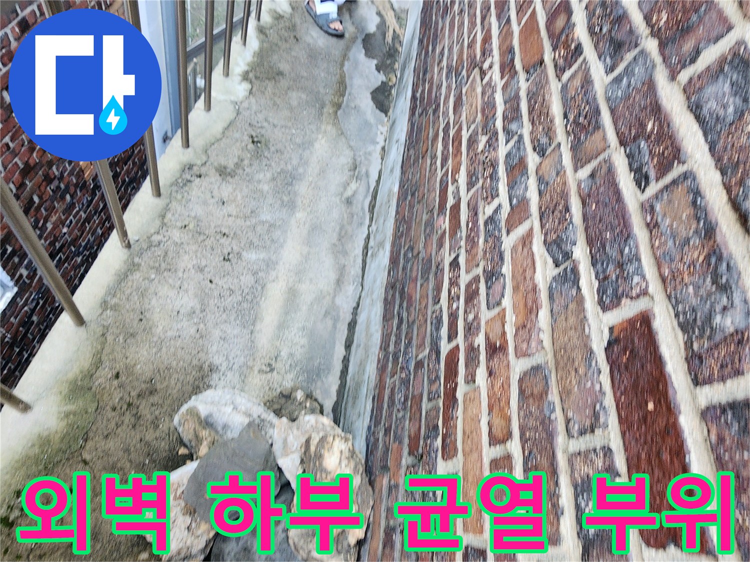 벽돌 벽면 아래쪽의 갈라진 틈과 거친 지면 상태를 보여줍니다.