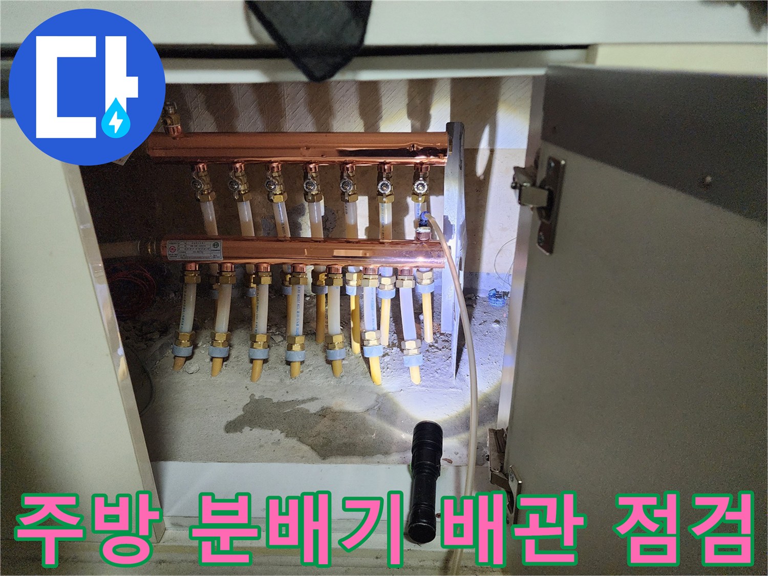 싱크대 밑 분배기 주변의 젖은 바닥과 배관들