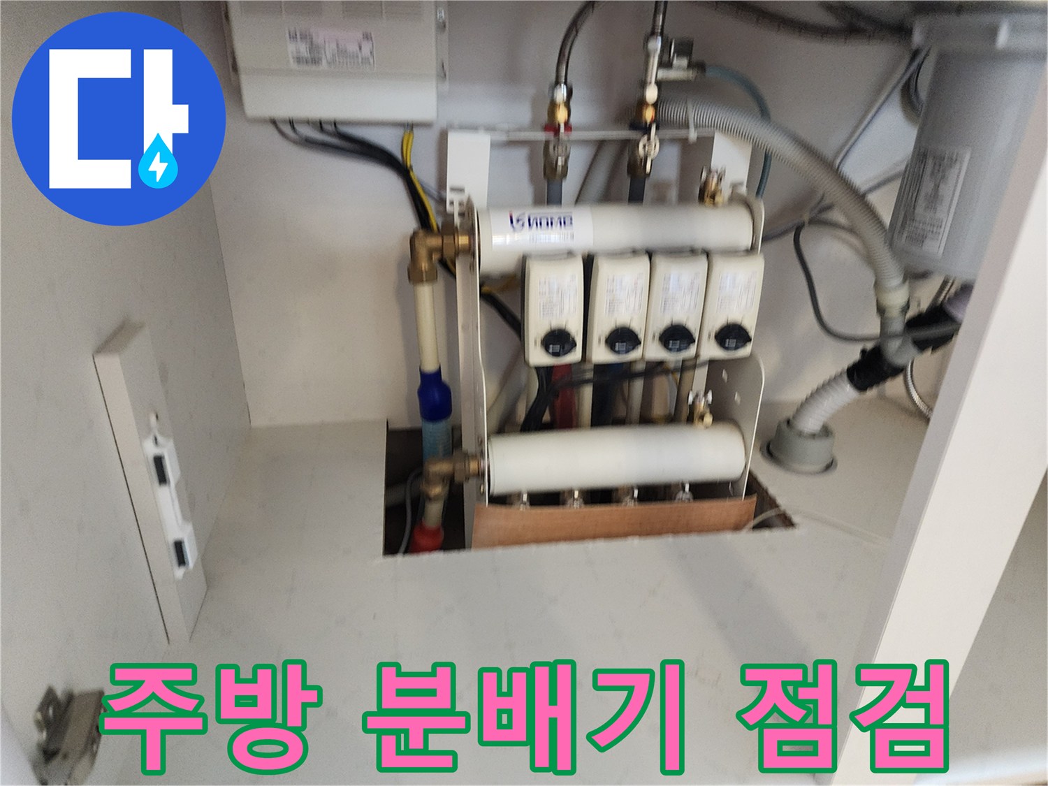 싱크대 하부장 내부의 급수 분배기와 연결 배관 상태를 확인하는 모습입니다.