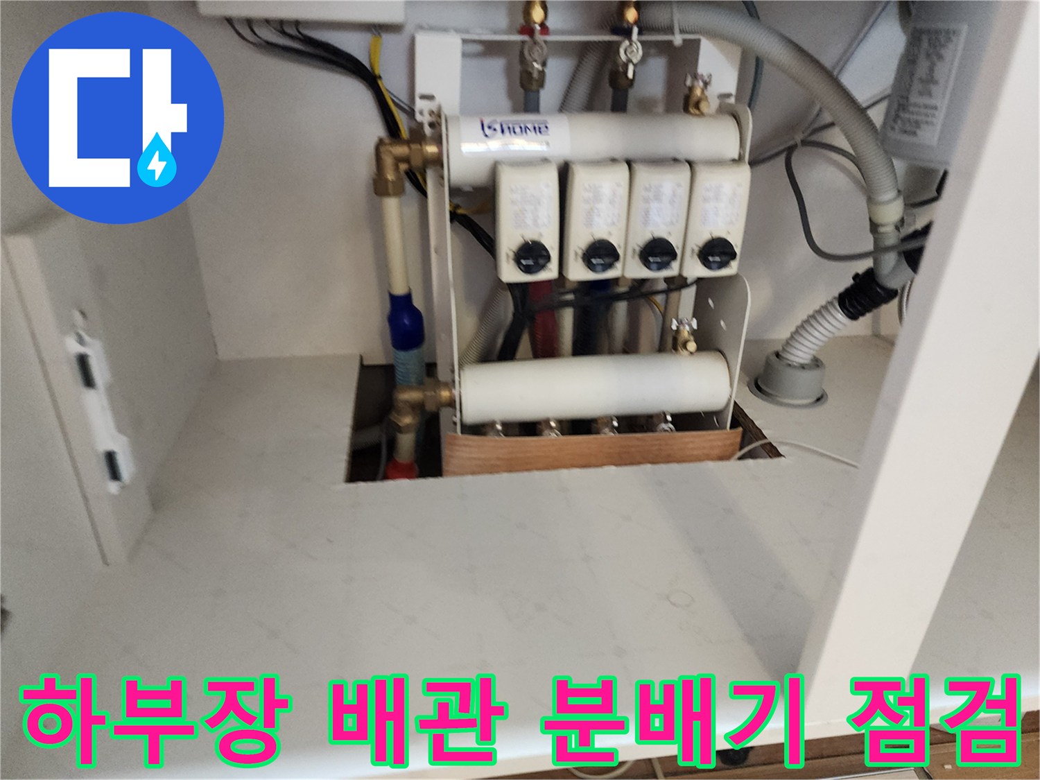 주방 싱크대 하단에 설치된 수도 분배기와 각종 연결 배관의 모습입니다.