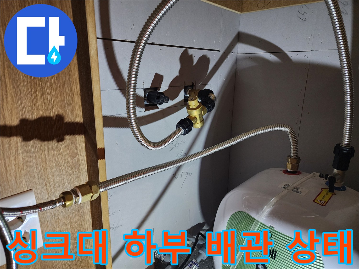 주방 하부장 내 전기 온수기와 연결된 금속 호스의 배치 모습