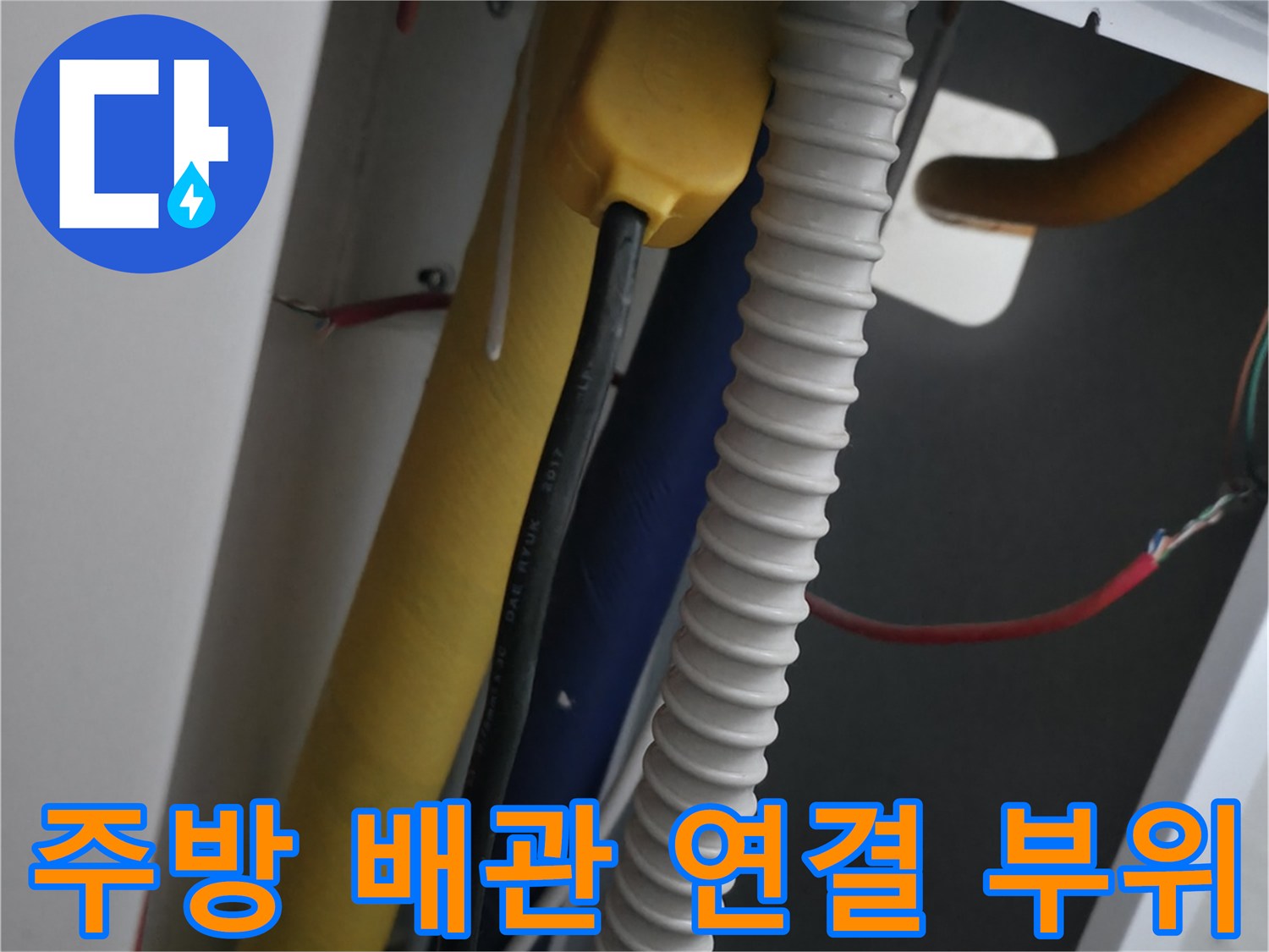 노란색 보온재 배관과 흰색 주름관이 교차하는 싱크대 하부 모습