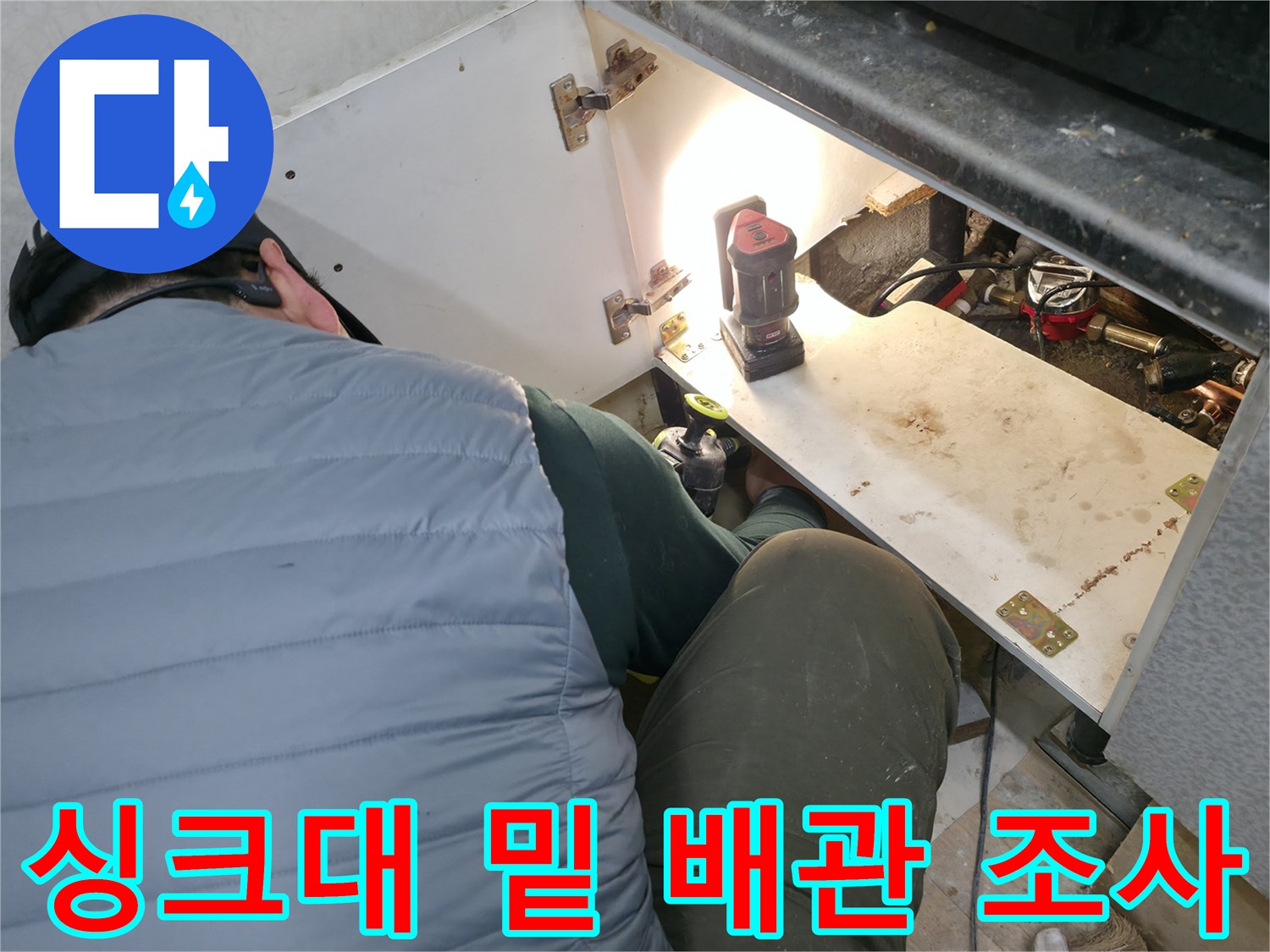 조명을 사용해 싱크대 하부의 복잡한 배관 구조를 점검하는 모습