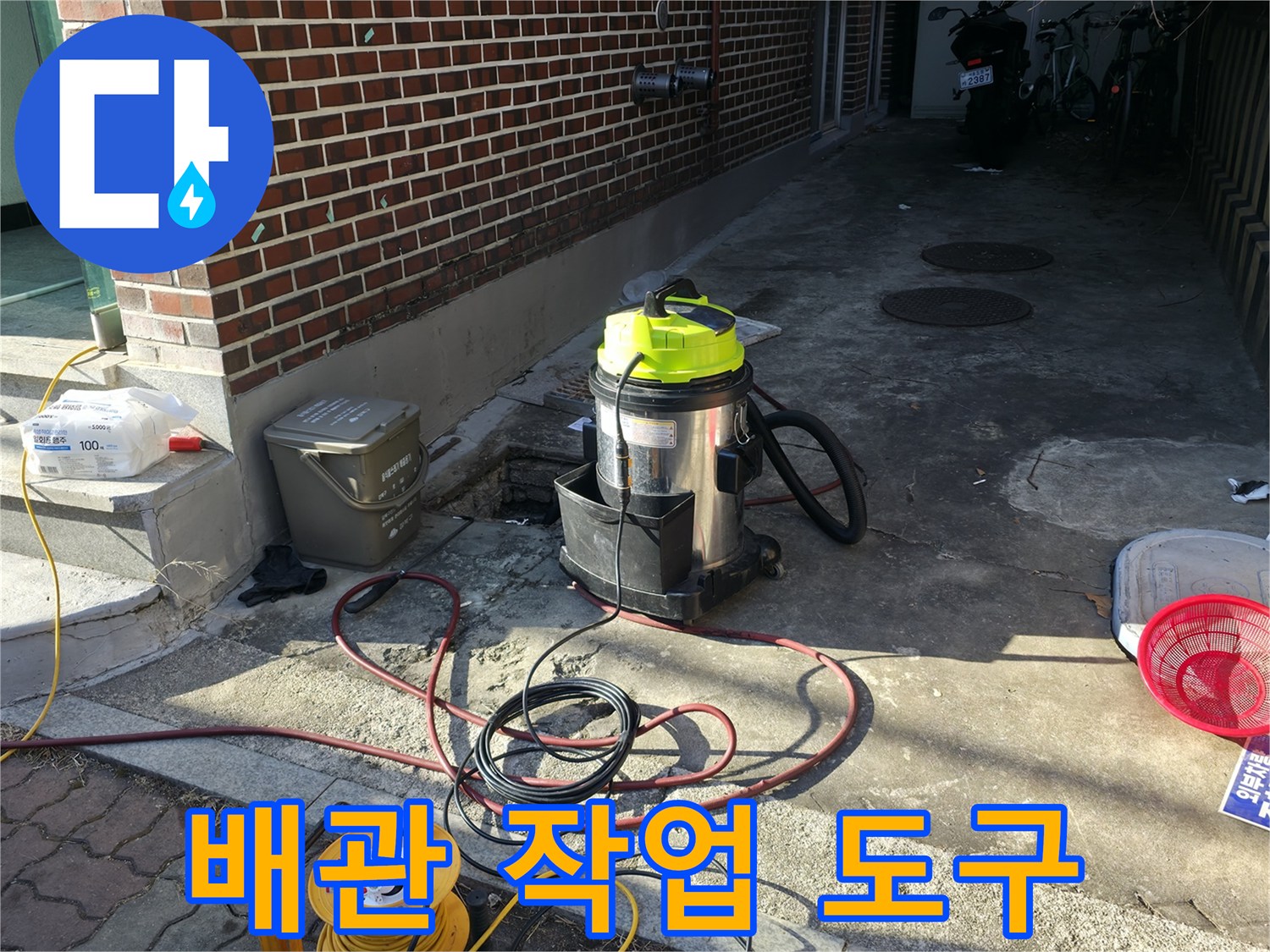 벽돌 벽 옆 통로에 놓인-작업용 청소기와 전원 케이블 뭉치