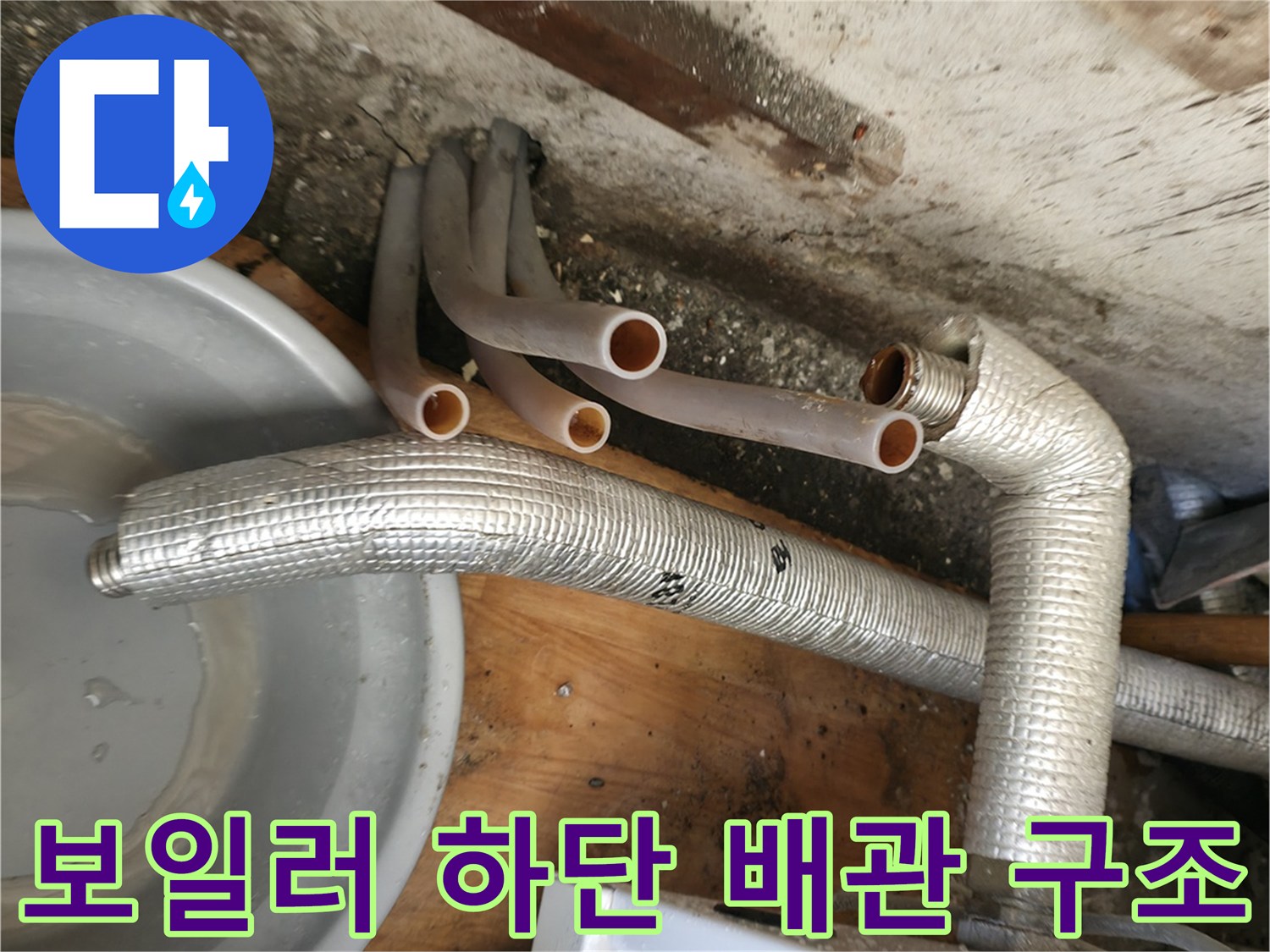 보일러 본체 아래로 뻗어 나오는 보온재 처리된 배관과 분지관의 모습입니다.