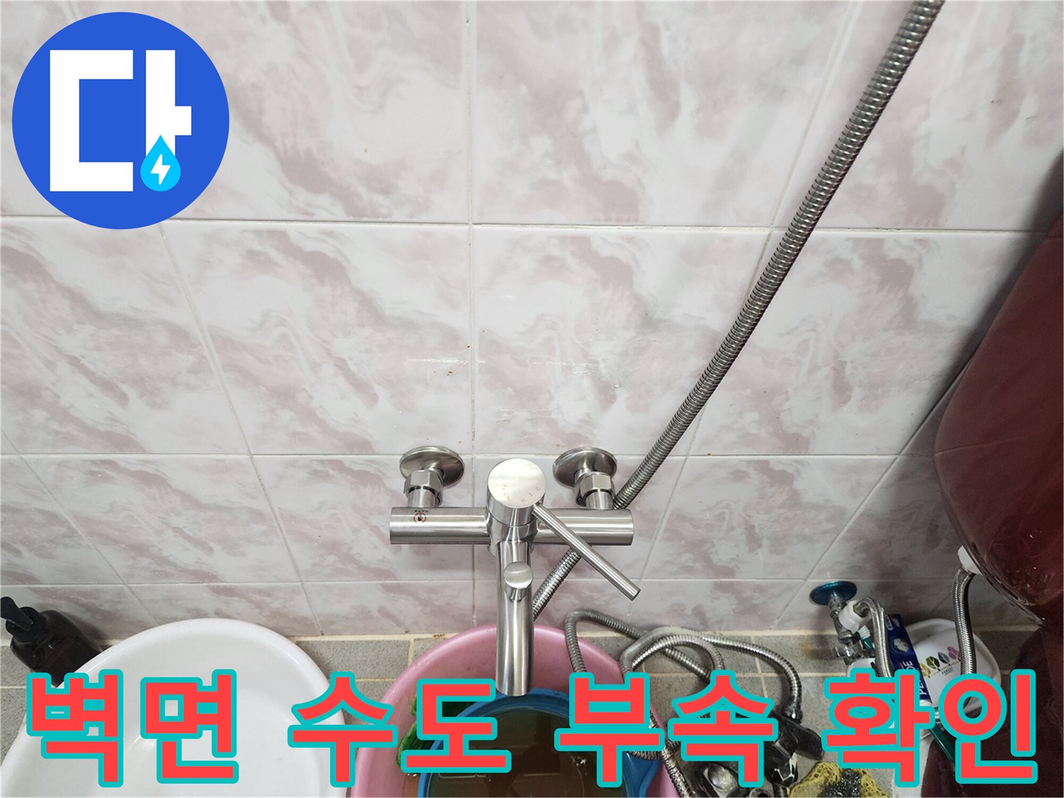 주방 타일 벽면에 노출된 수도 밸브와 연결 호스의 상세 모습입니다.