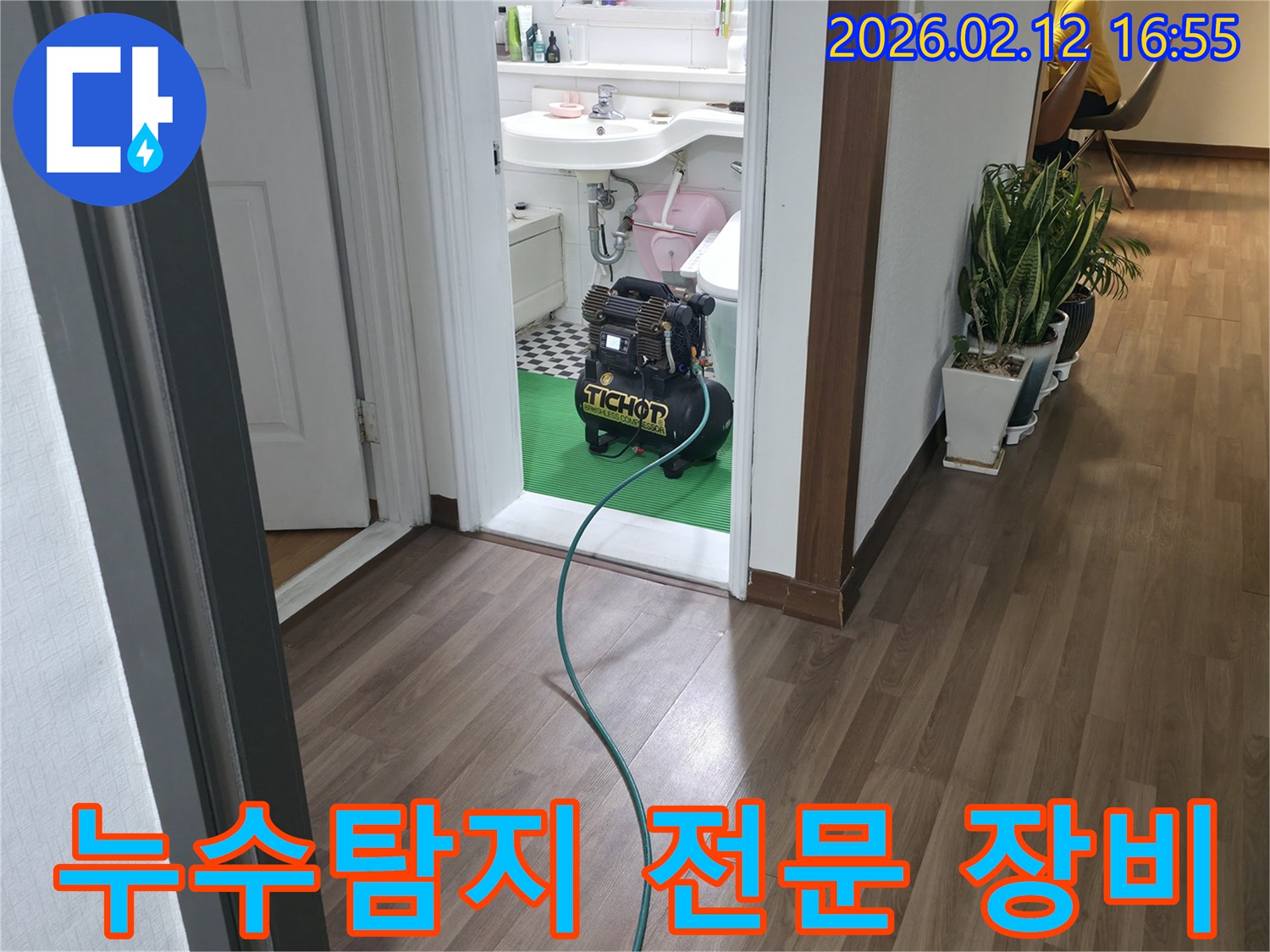 욕실 문턱에-놓인 누수-탐지용 압력-장비에서-녹색 호스가-연결되어-정확한 누수-탐지를 위한-준비 과정