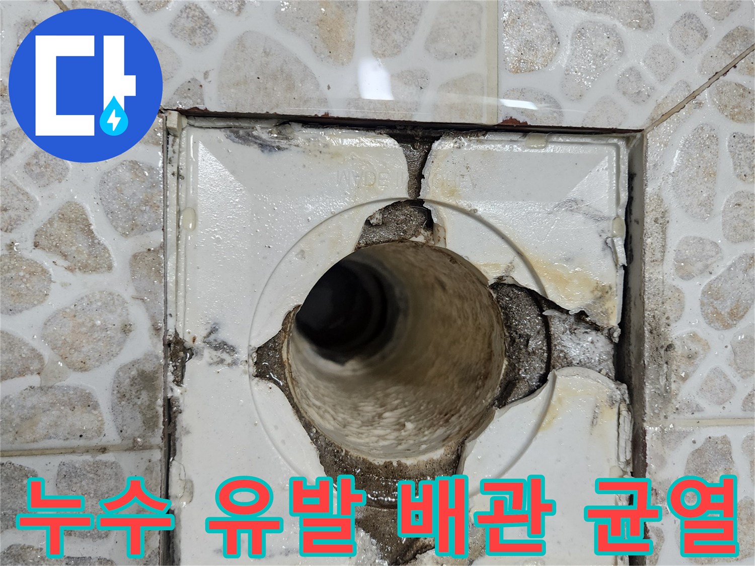 배수구 주변의 갈라진 타일과 노출된 배관 입구