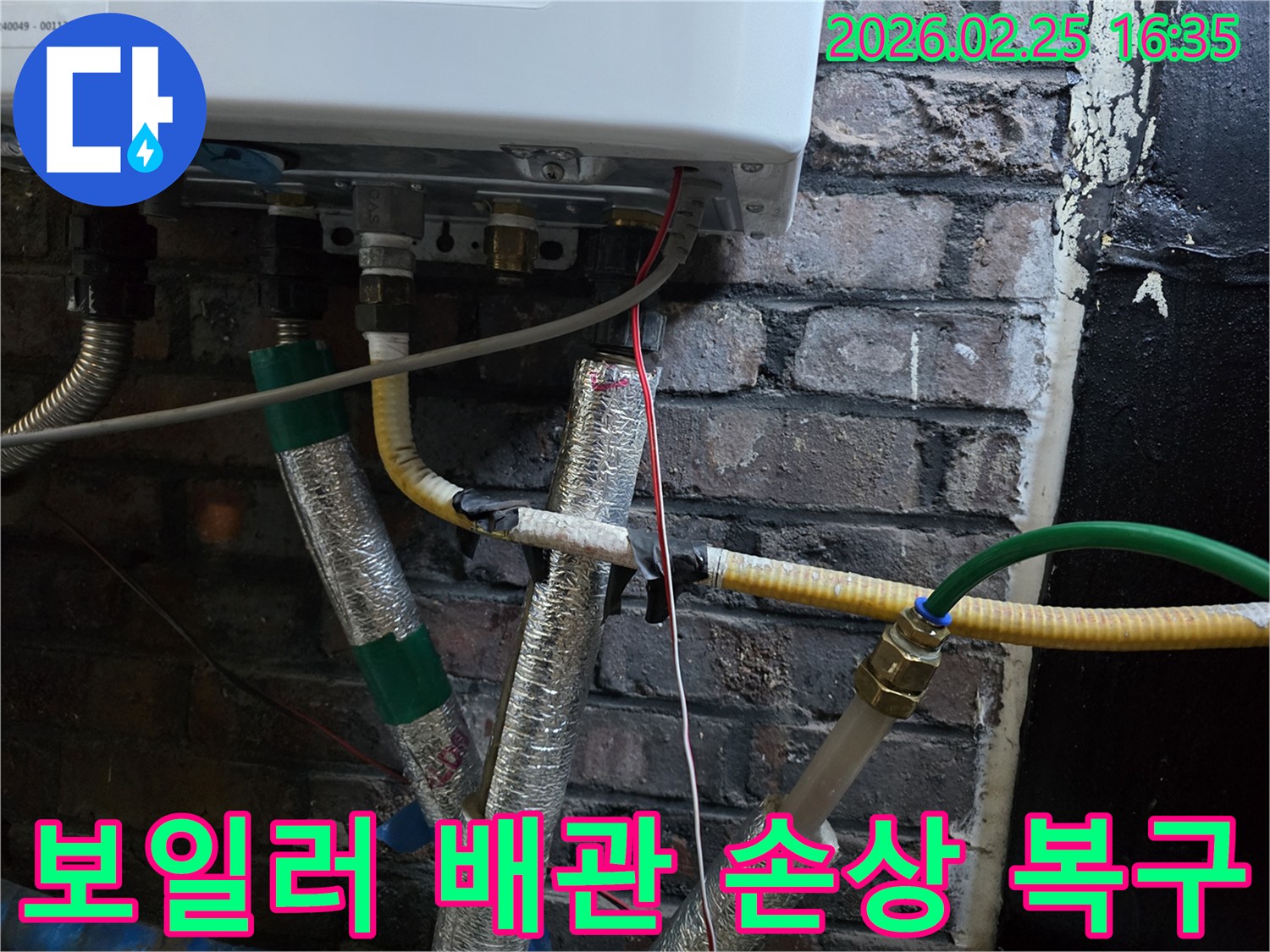 이 이미지는-벽에 설치된-보일러 하단부의-복잡한 배관 연결부와-전선-그리고-은색 단열재로-감싸진-파이프들을-보여주며-누수 피해로 인한-배관 손상 복구를-위한-점검이-진행되고-있음을-암시합니다.