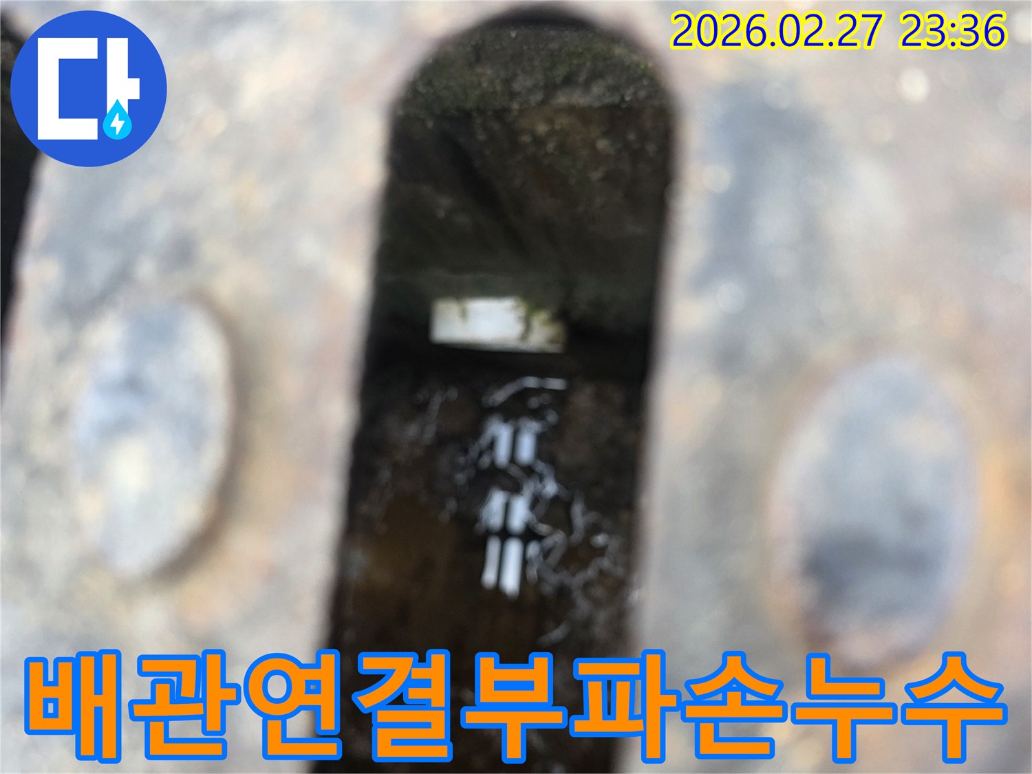 녹슨-철제-덮개-아래-고인-물과-물속에-잠긴-파손된-배관-연결부가-보이는-누수-현장