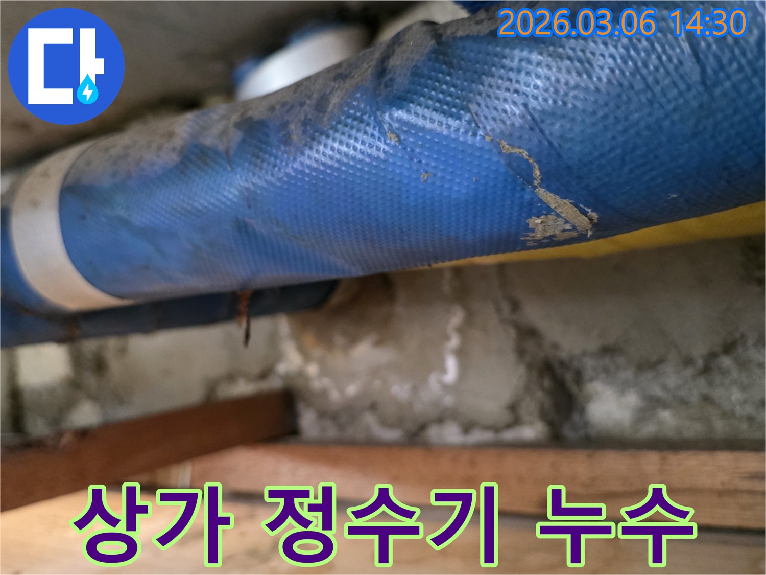 상가 건물 내부-파란색 정수기 배관과-젖은 콘크리트 벽면-그리고 나무 지지대를-정밀하게 점검하는 모습