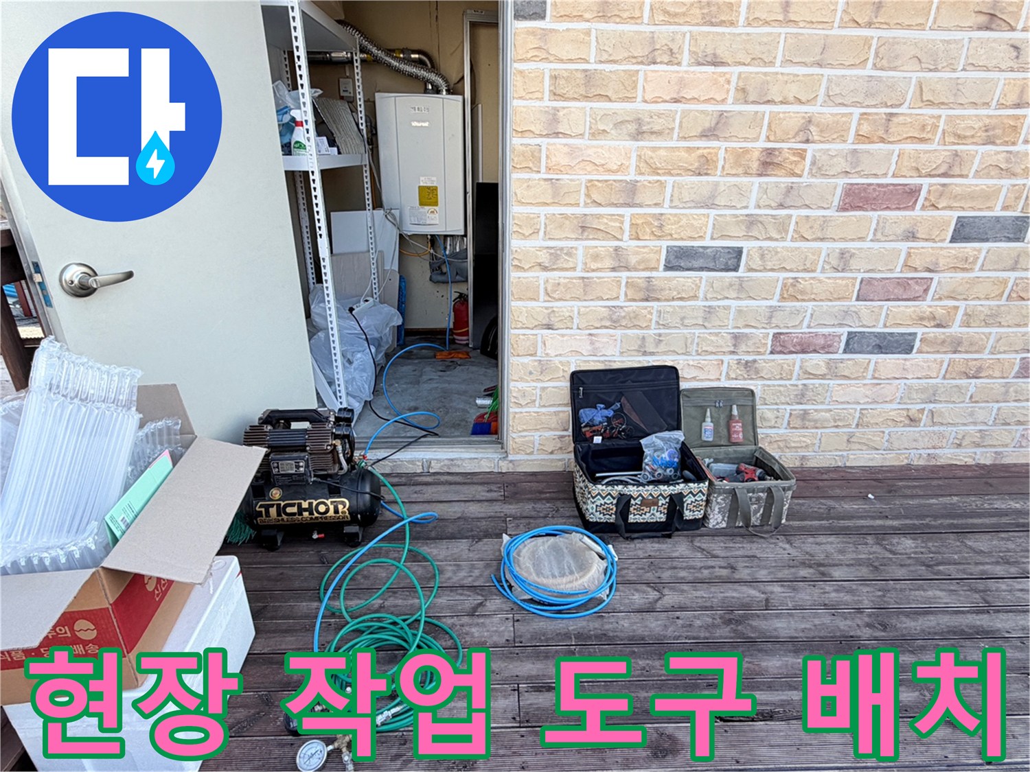 벽돌 무늬 외벽 앞 테라스에 놓인 누수 점검용 콤프tes샤와 각종 수리 자재들입니다.