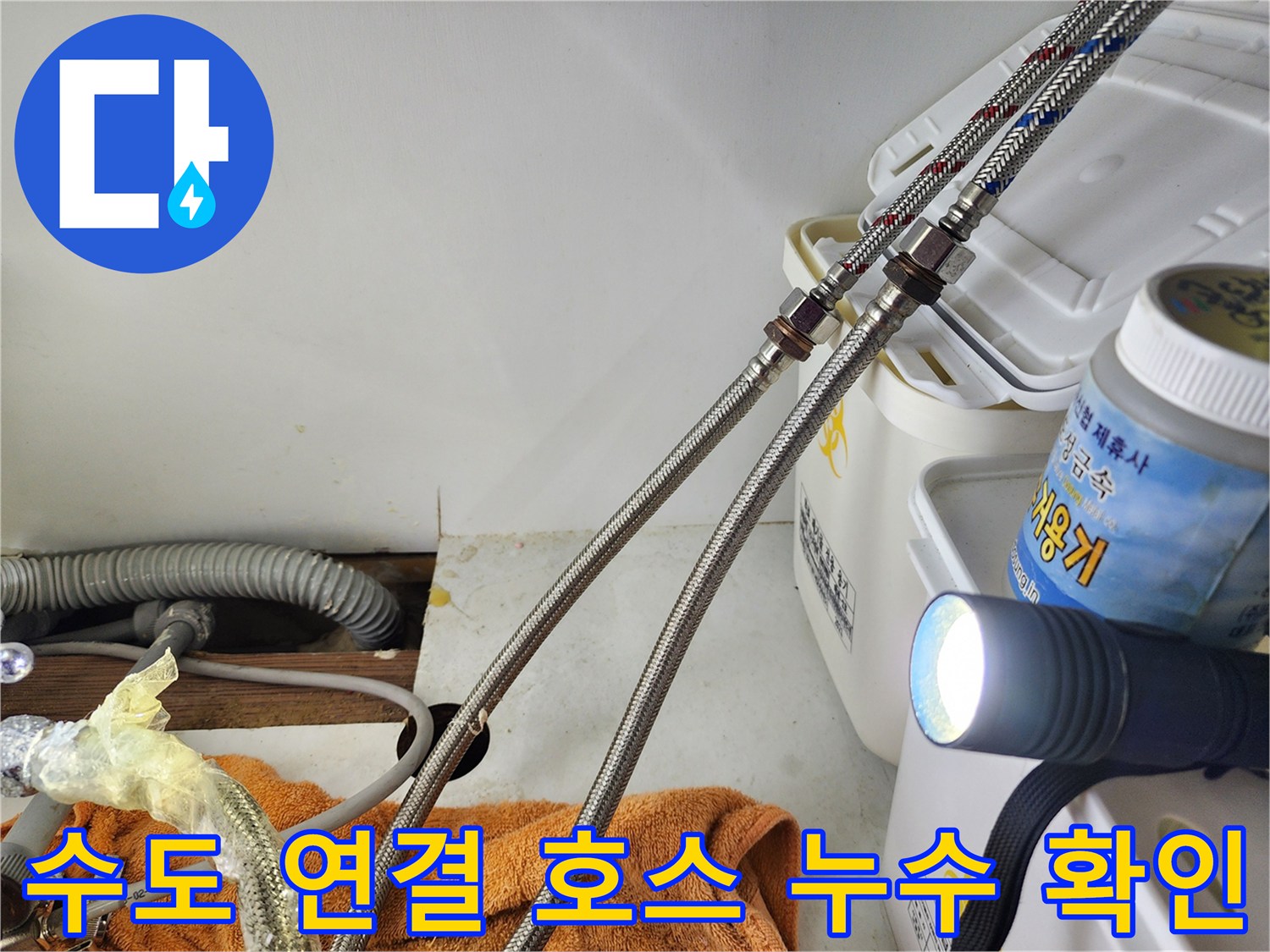 어두운 싱크대 밑 공간에서 고압 호스의 금속 캡 부위를 비추는 손전등 빛