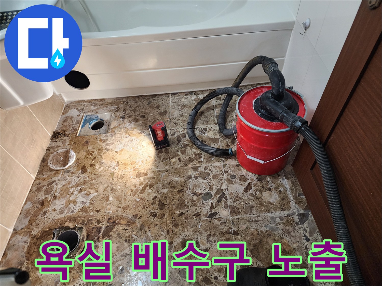 공사 중인 욕실 바닥의 배수관 입구와 빨간색 청소기