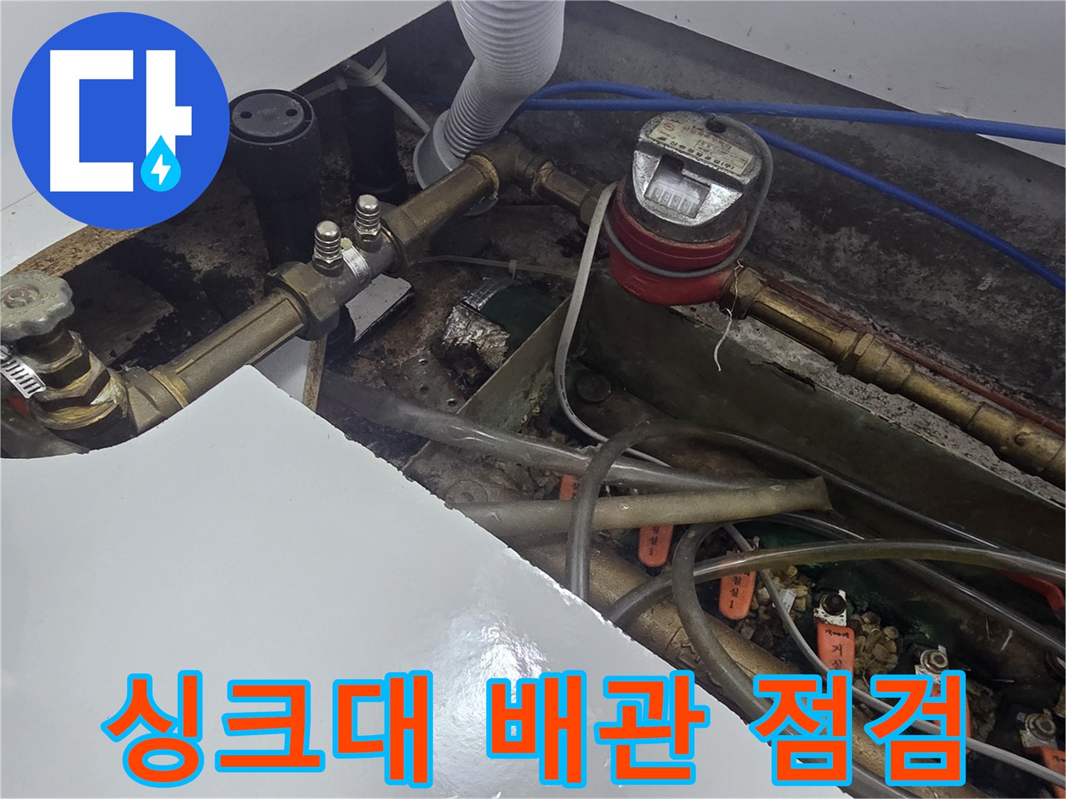 주방 싱크대 아래 계량기와 복잡한 배관 구조를 보여주는 사진입니다.