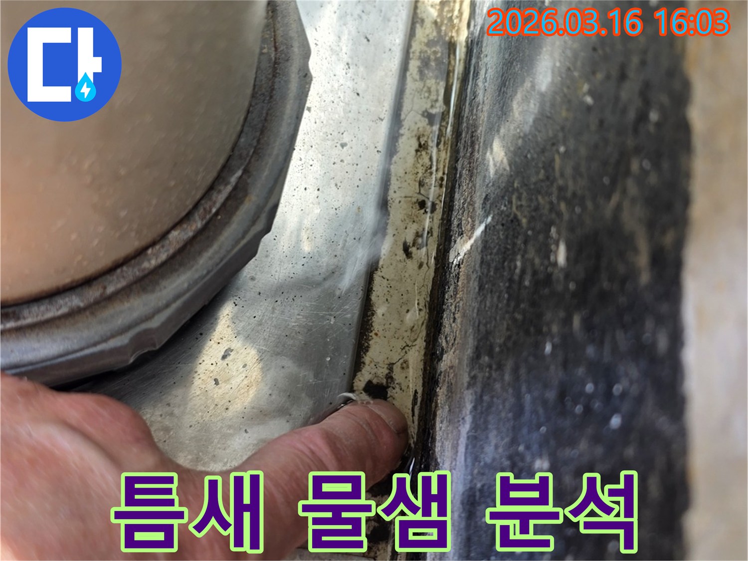 Close-up view of a hand identifying a subtle water leak in a building's structure- possibly near a pipe or window.