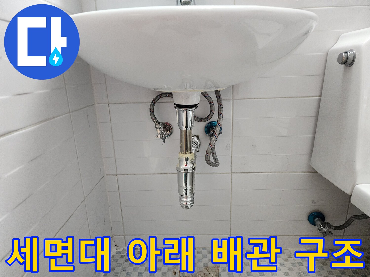 세면대 하단 벽면 타일과 수도 배관이 보이는 현장 사진입니다.