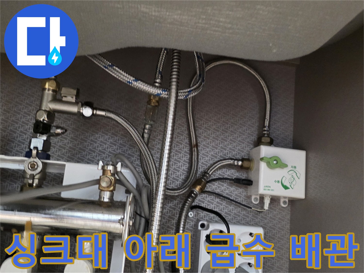 주방 싱크대 하단에 설치된 금속 분배기와 급수 호스 연결부