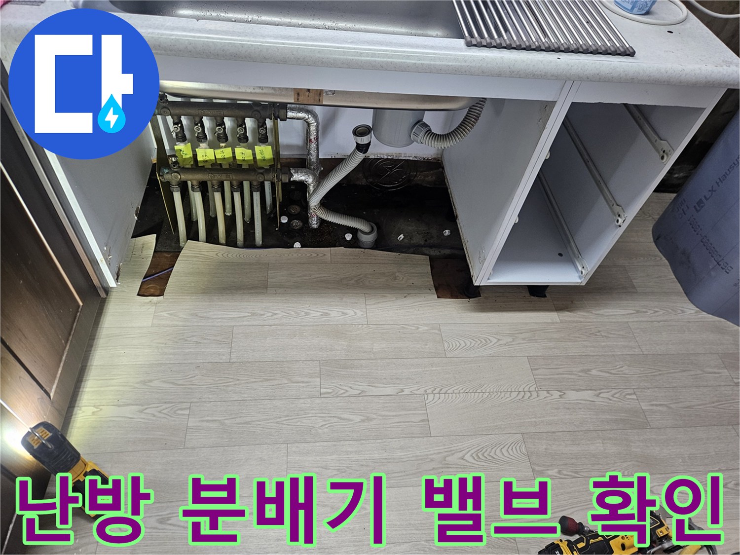 싱크대 아래 공간에 노출된 난방 분배기 밸브와 연결 배관들