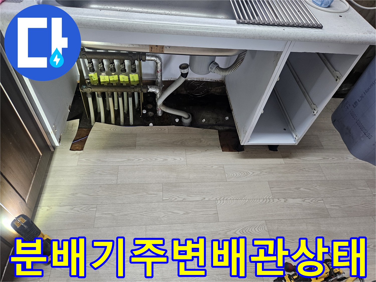 싱크대 아래 분배기 주변의 젖은 바닥과 노출된 배관들