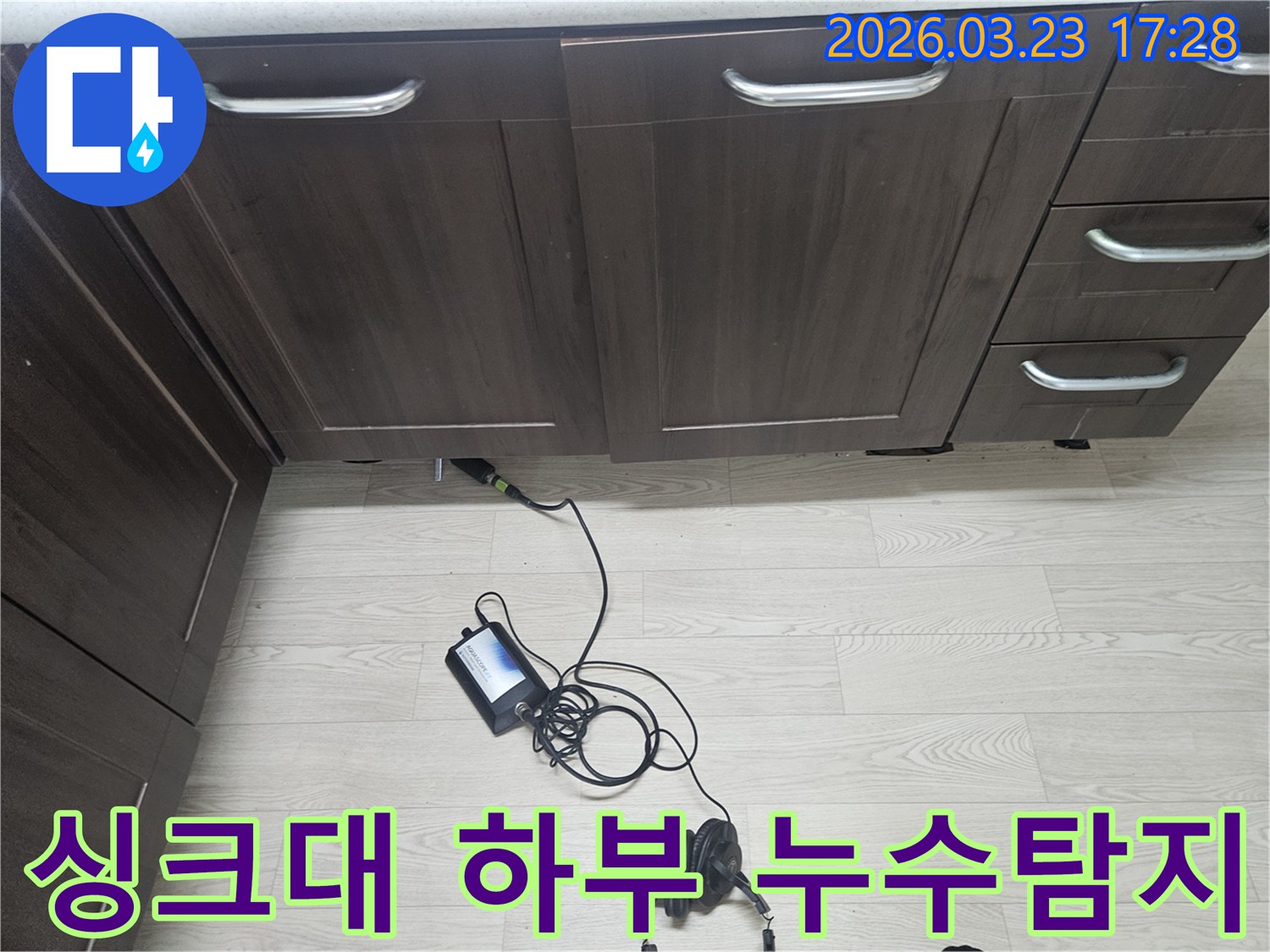 주방 싱크대 아래에서 발생한 누수를 정확히 찾기 위해-전문 장비를 활용하여-누수탐지 엔지니어가 작업 중인 모습