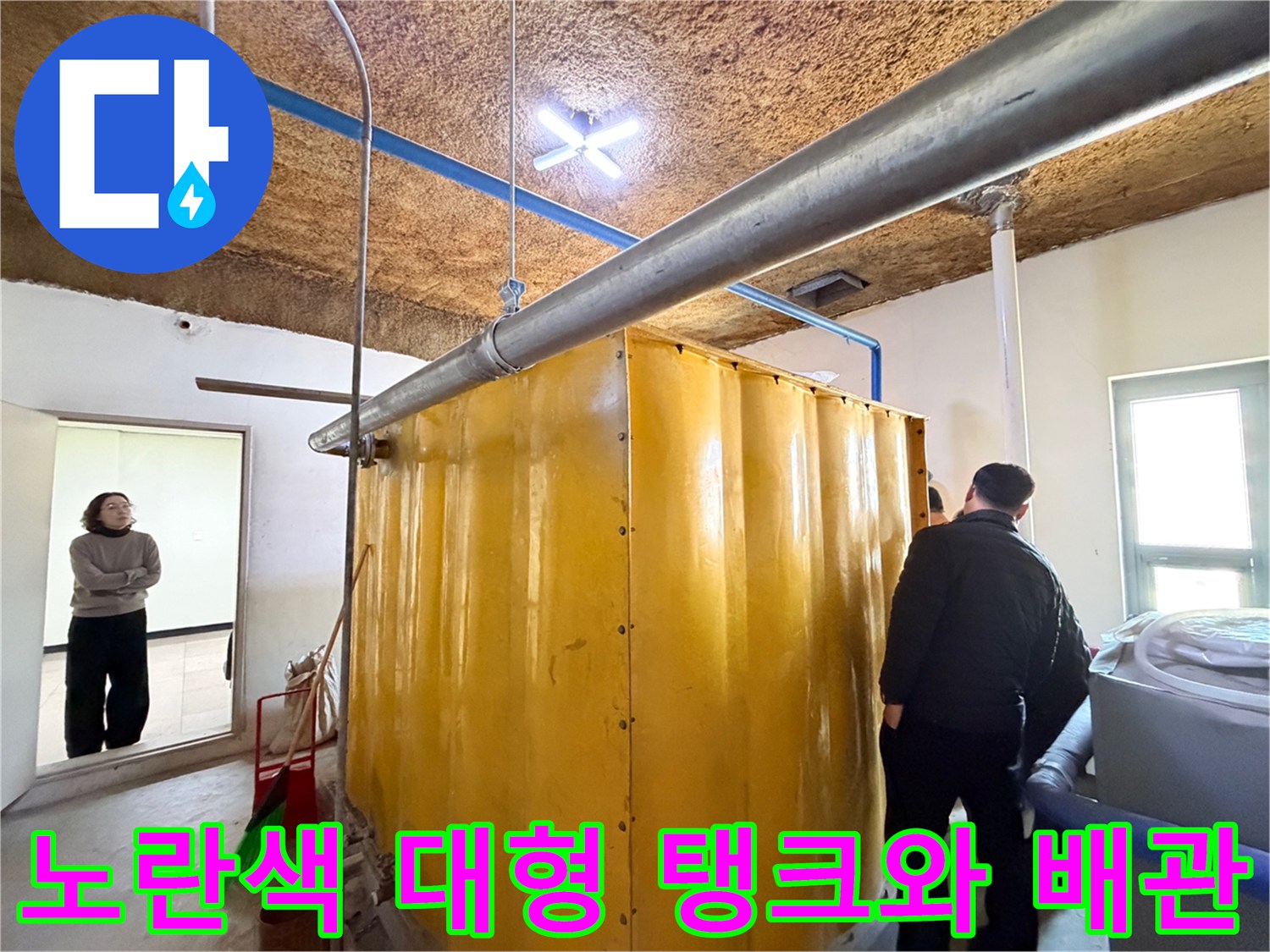 지하 주차장 내 설치된 노란색 수조와 상부 금속 배관의 모습입니다.
