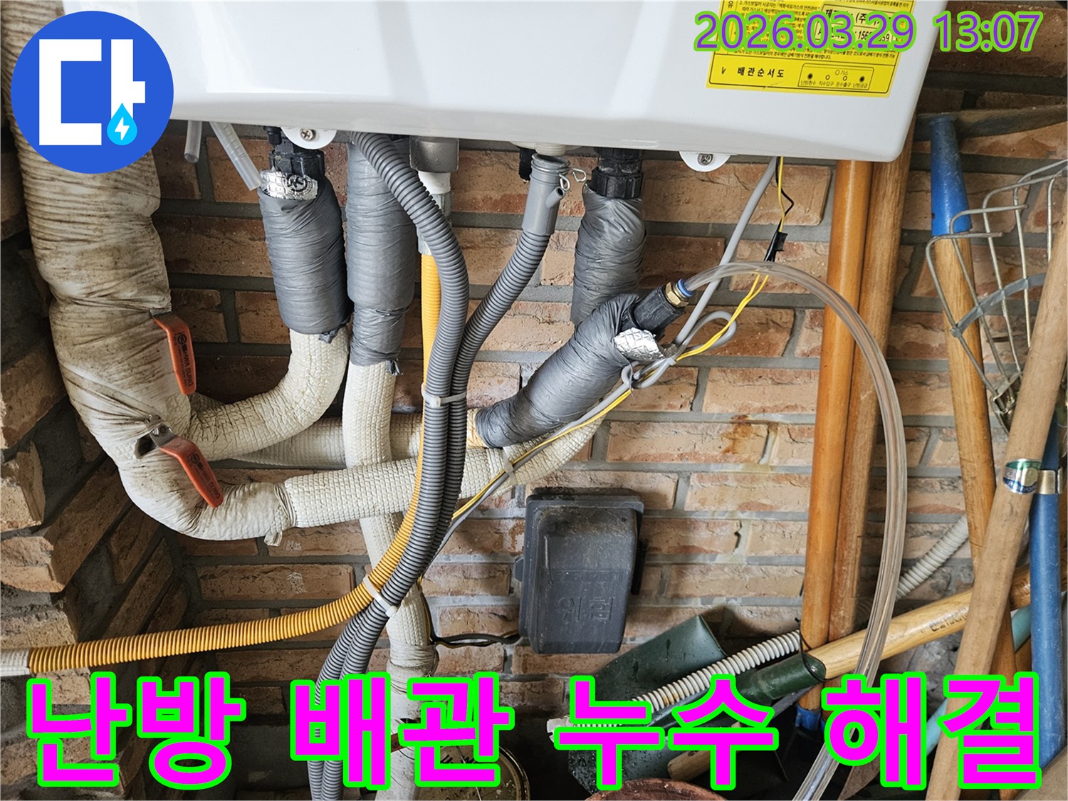 벽돌 벽에 설치된 난방 배관들이-회색 단열재로 감싸져 있으며-겨울철 누수 문제를 해결하기 위한 점검이 이루어지고 있습니다.