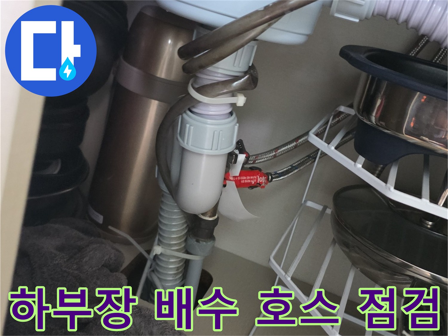 싱크대 하부장 내부에 연결된 흰색 배수 호스와 부속품들입니다.