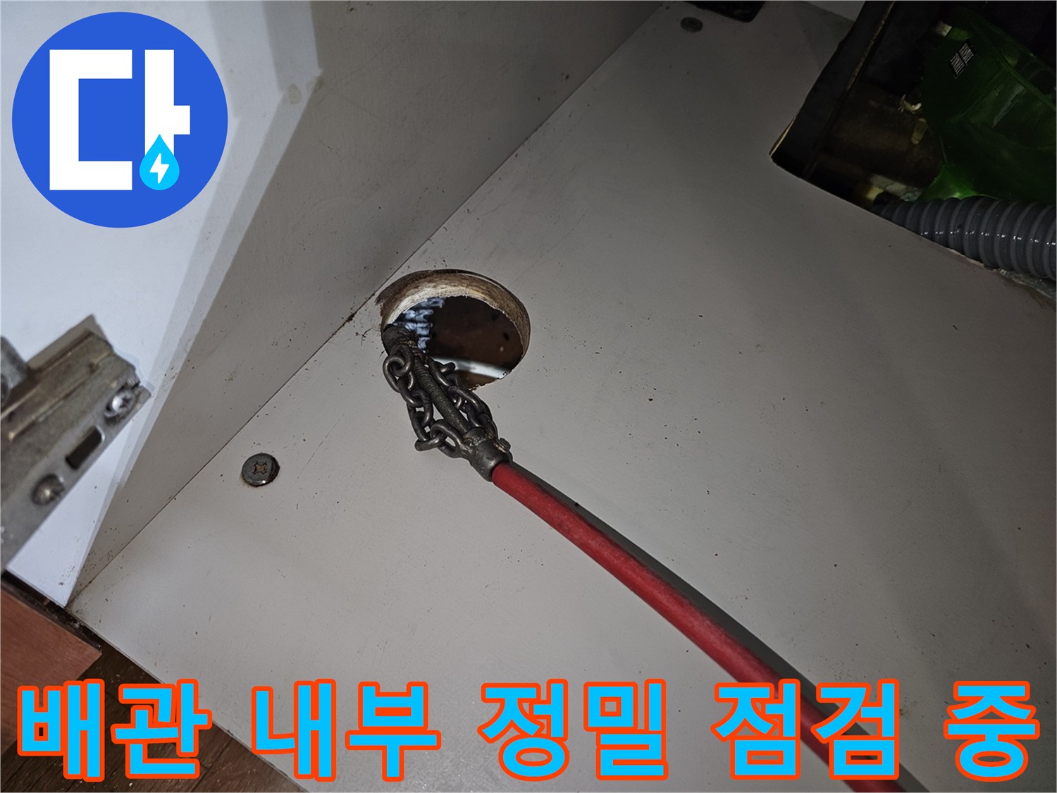 붉은색 케이블이 연결된 내시경 카메라를 배관 입구로 밀어 넣는 장면입니다.