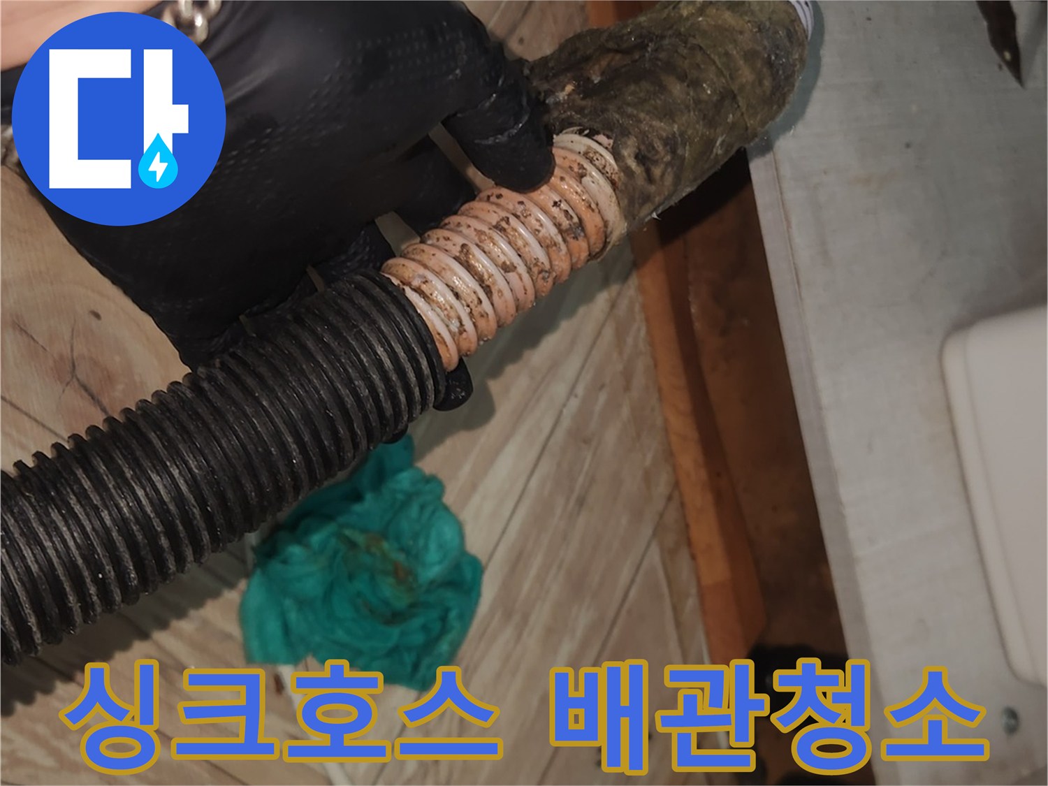 검은 장갑을 낀 손이-오랜 사용으로 찌꺼기가 쌓인 싱크대 배수 호스를-꼼꼼히 확인하며-석션 클리닝을 준비하는 모습