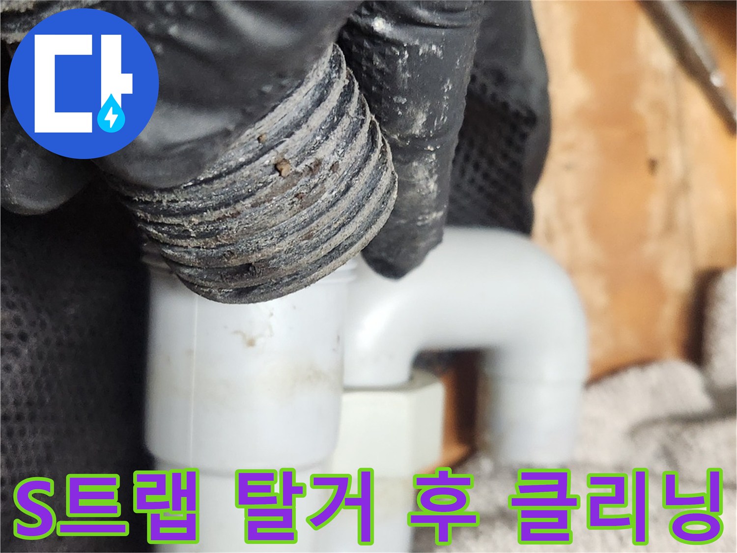 검은색 작업 장갑을 낀 손이-오래된 S트랩 배관을 조심스럽게 분리하여-내부 이물질을 제거하는 모습입니다