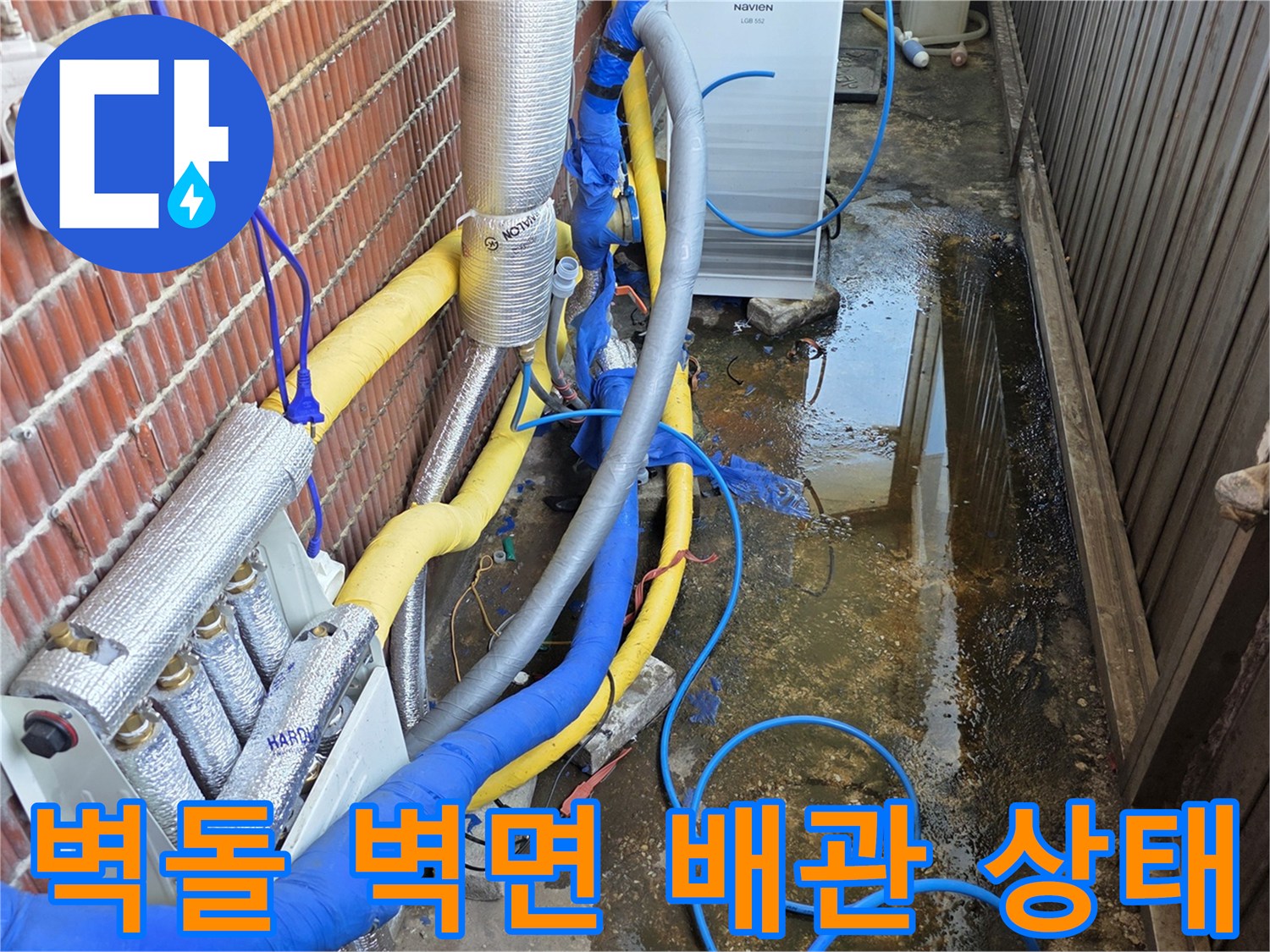 벽돌 외벽에 설치된 은색 보온재 배관과 파란색 유연 호스