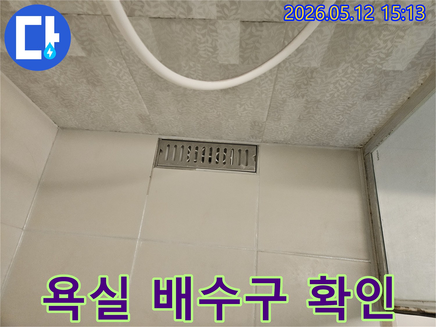 욕실 바닥에 설치된 스테인리스 선형 배수구와-주변의 흰색 타일-그리고 천장 마감재가 보이는-누수 점검 현장의 모습입니다.