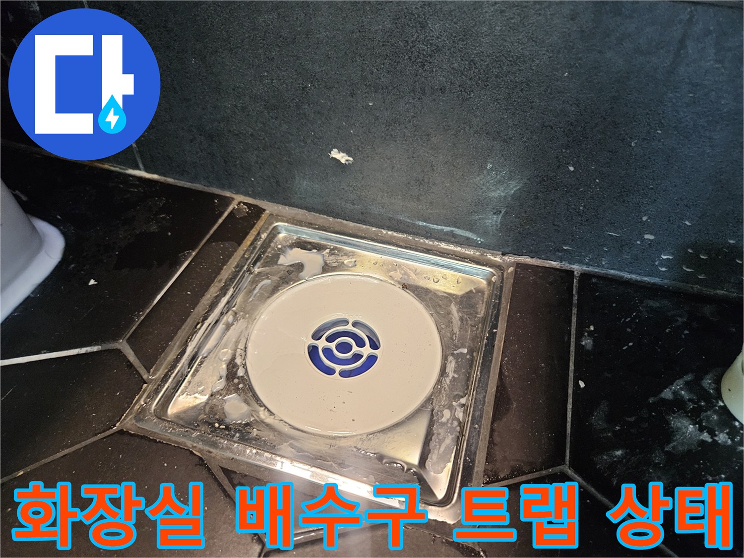검은색 타일 바닥에 설치된 하얀색 배수구 트랩과 주변의 오염된 모습