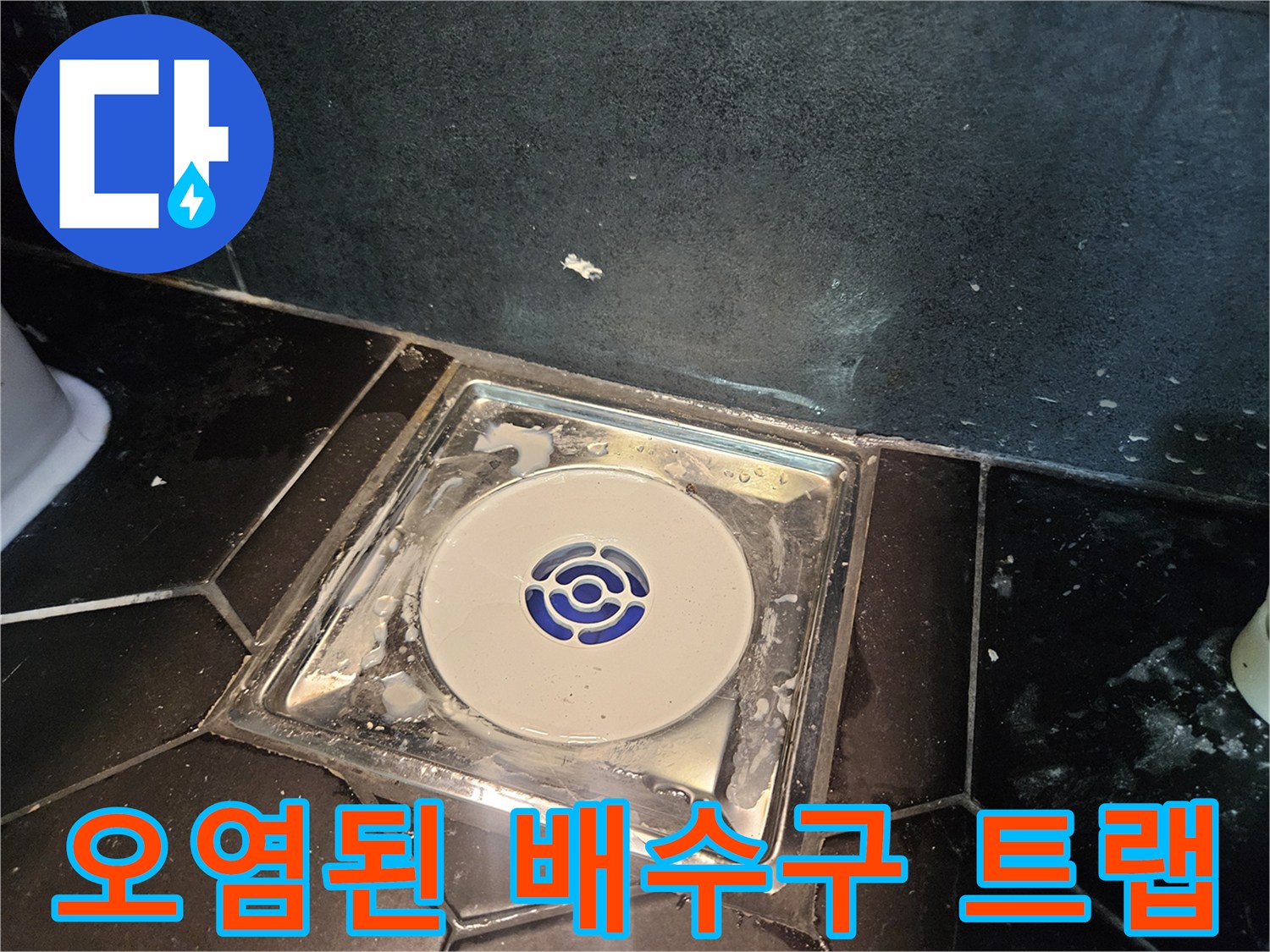 검은색 타일 바닥에 설치된 흰색 배수 트랩과 주변 물때