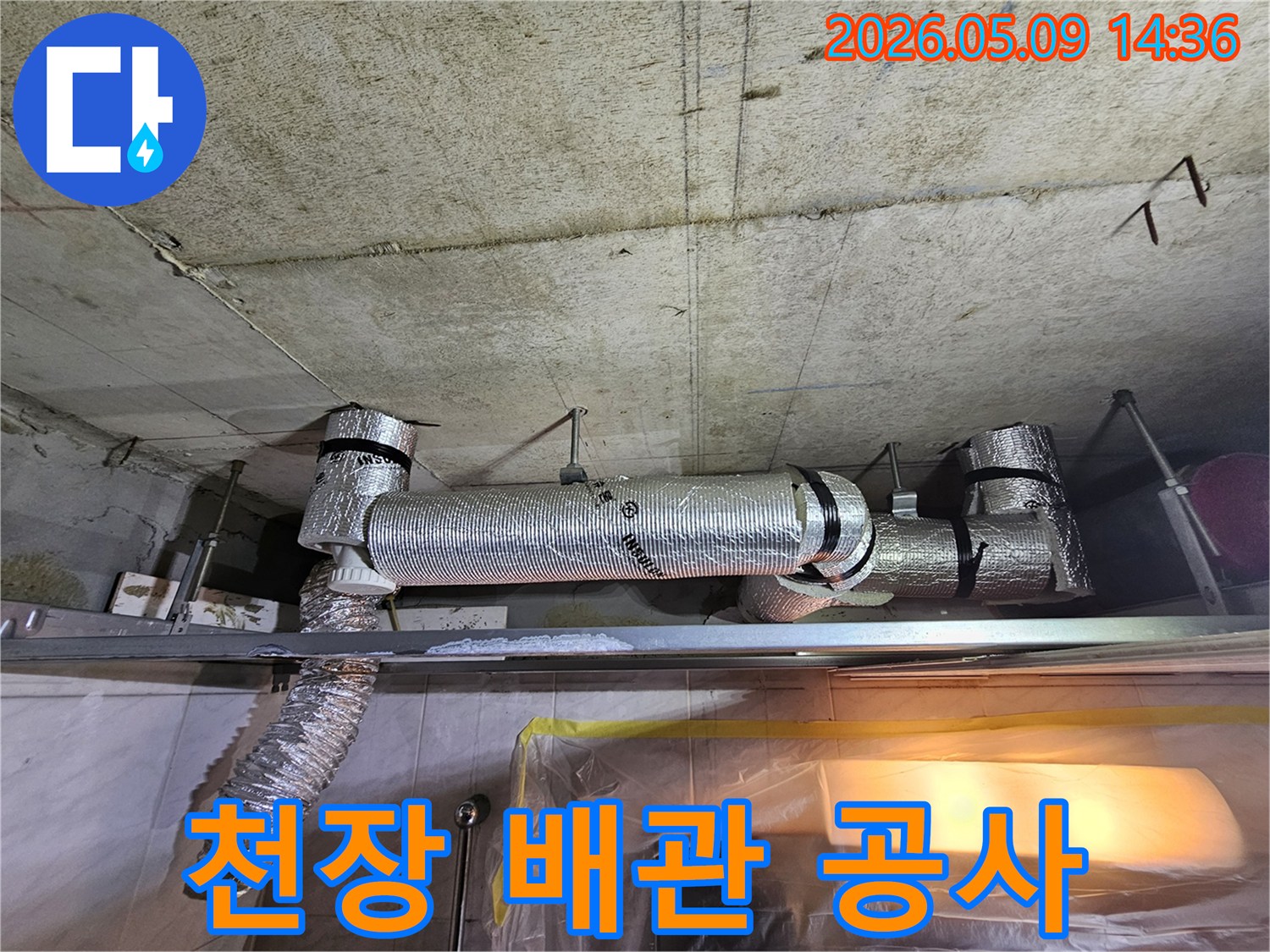 천장 콘크리트 구조물 아래에 설치된-단열 배관과 유연한 덕트의 공사 진행 상황을 보여주는 이미지입니다.