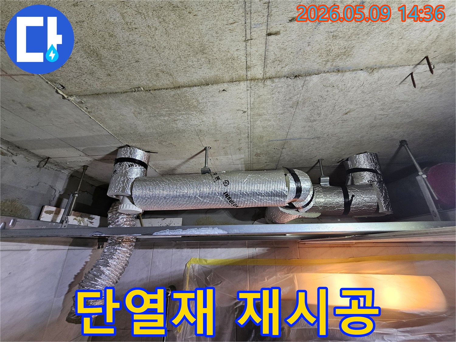 천장 콘크리트 아래에 설치된-배관의 단열재를 재시공하거나 보강하는 공사 현장의 이미지입니다.