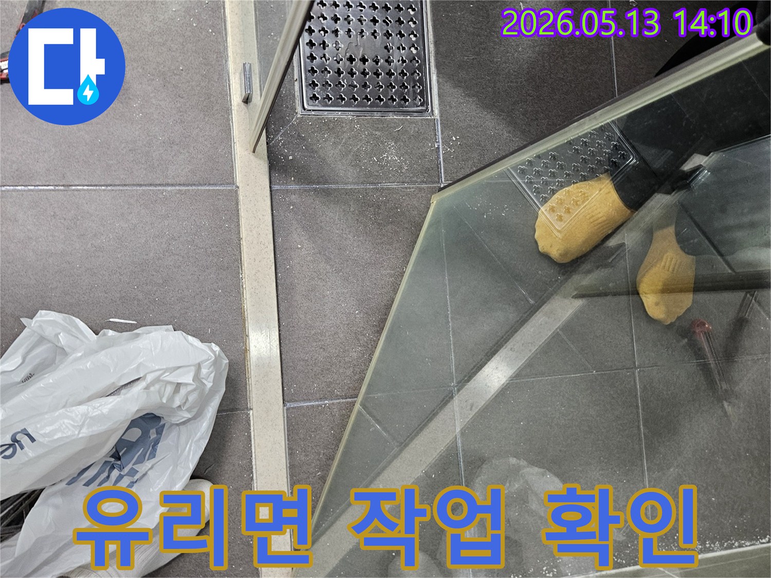 샤워 부스 유리면에 비친-작업자의 모습과 주변 환경을 통해-누수 보수 작업의 진행 상황을 확인하는 현장입니다.