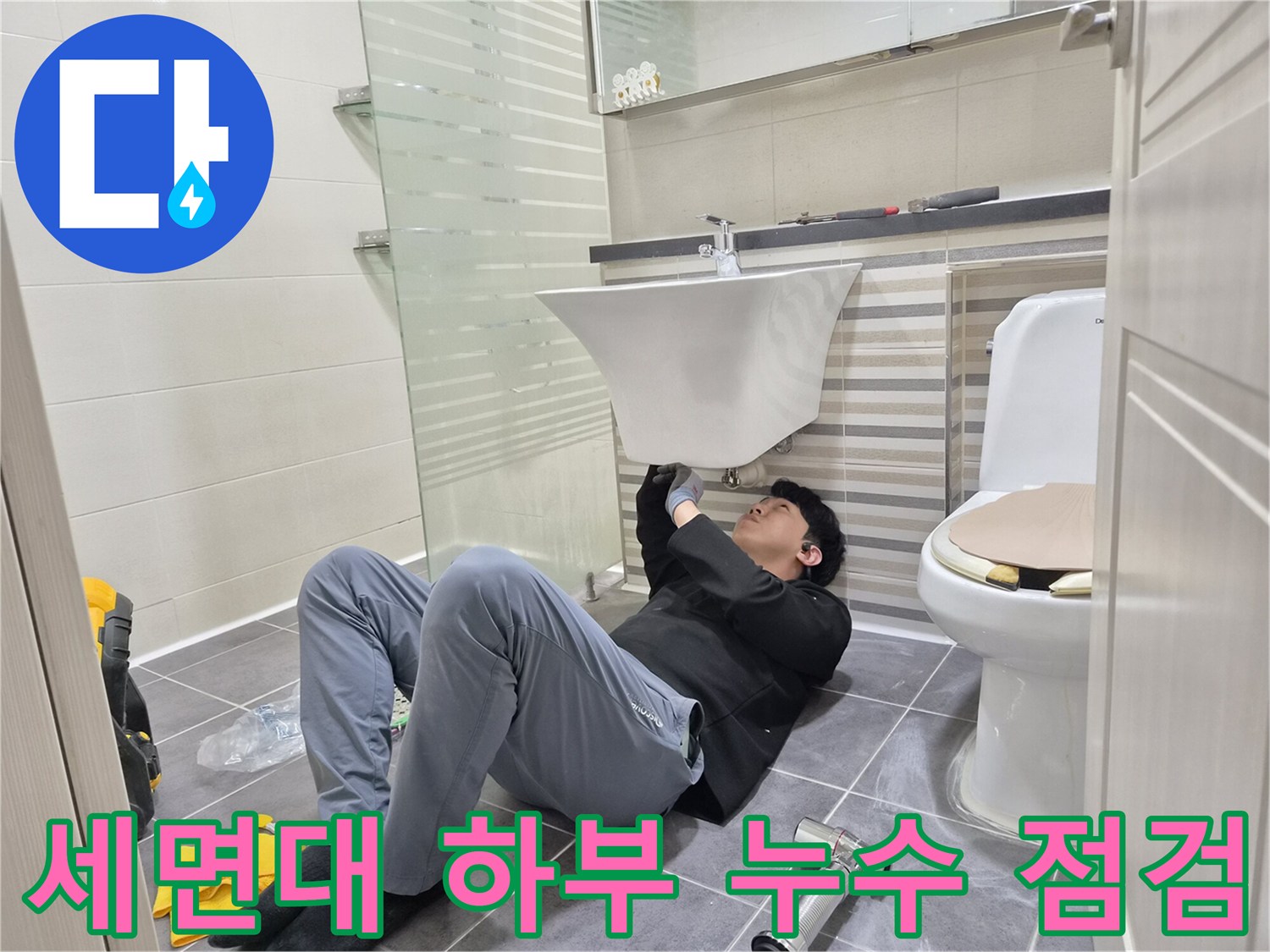세면대 아래쪽 좁은 공간에서 배관 연결 상태를 검사하는 모습