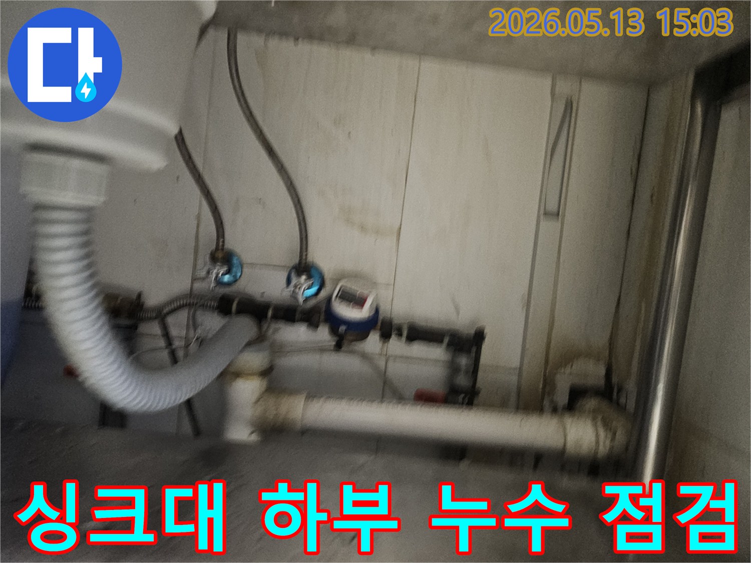 싱크대 아래-복잡한 배관과-수도 계량기-그리고 누수 흔적을-보여줍니다.