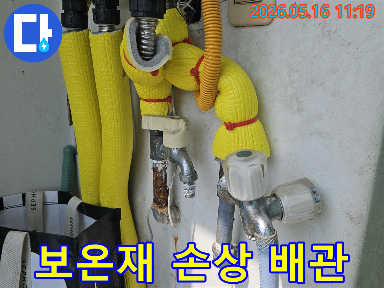 이 이미지는-강동구 길동 아파트 베란다에서-보온재가 손상된 배관을-전문가가 점검하며-누수 및 동파 위험을-진단하는 현장을 보여줍니다.