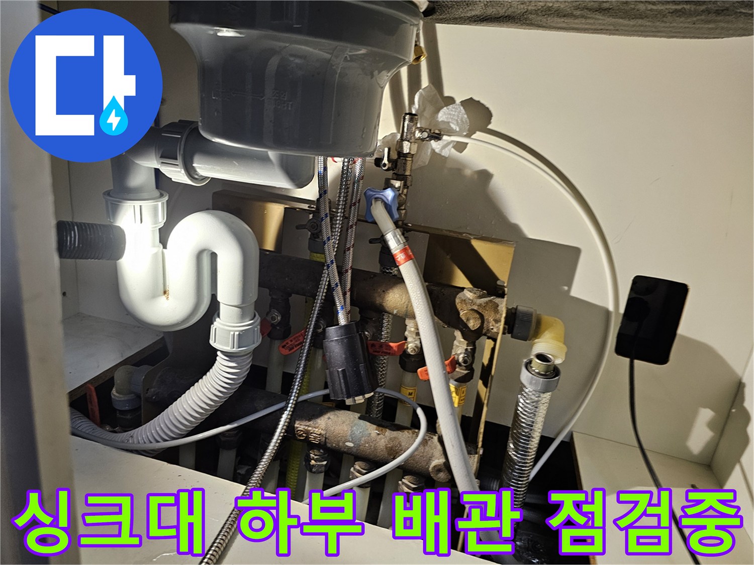 싱크대 밑부분의 복잡한 배관 및 급수 호스 연결 구조