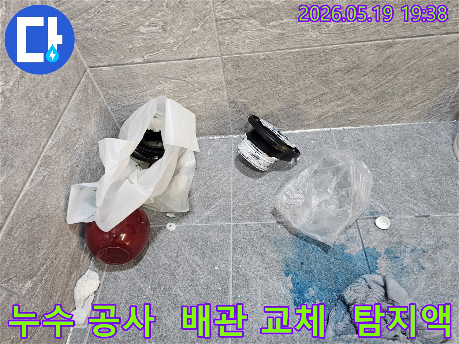 누수 공사 현장에서-파란색 탐지액으로 확인된 누수 지점과-교체된 배관 부품들이 바닥에 놓여 있습니다