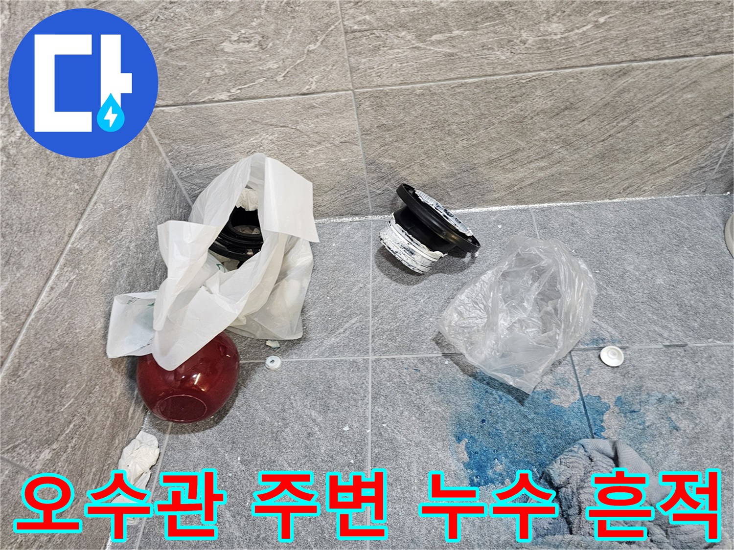 타일 바닥에 푸른색 얼룩과 함께 배관 부속이 놓여 있는 모습입니다.