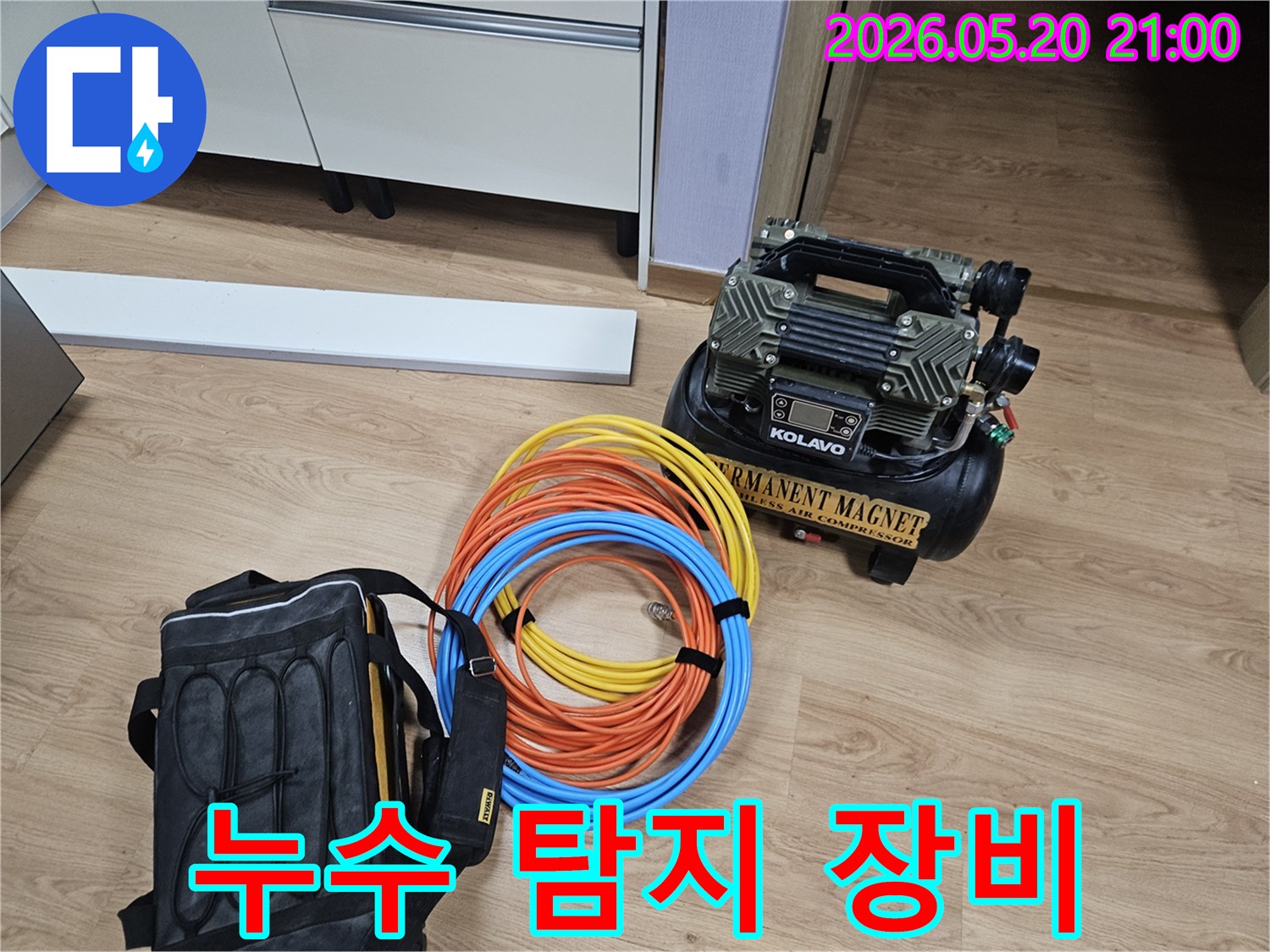 베란다 누수 탐지를 위해 준비된-에어 컴프레서와 다양한 색상의 호스-공구 가방이 바닥에 놓여 있습니다.